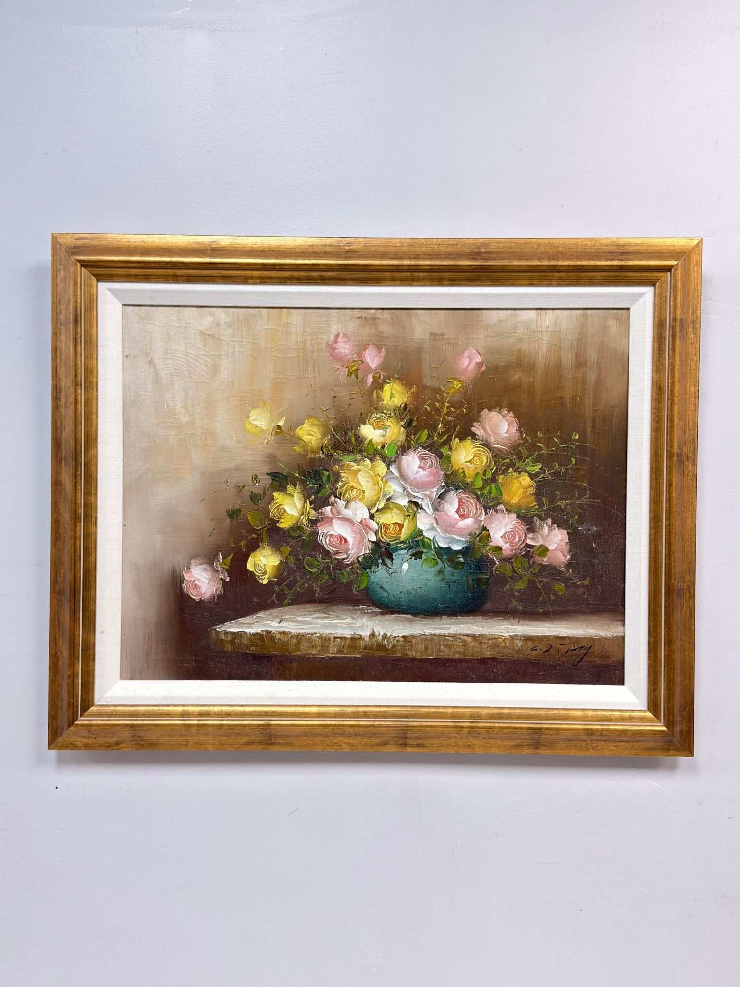 Framed Oil on Canvas Still Life Floral, Signed: The composition features a lush arrangement of pink and yellow roses contained within a teal-colored ceramic bowl, positioned on a neutral-toned ledge. The work is executed in a decorative mid-to-late