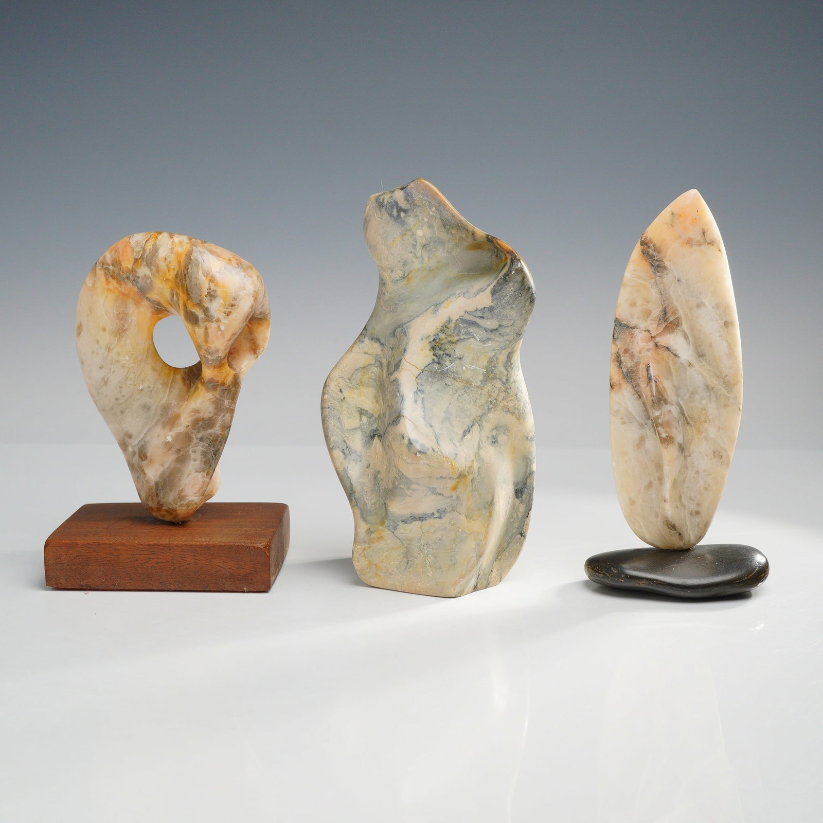 3pc Abstract Biomorphic Stone Sculptures: This trio of abstract biomorphic stone sculptures features organic, rounded forms carved from mottled beige, gray, and ocher-veined stone. Each piece is finished with a smooth, polished surface. The l