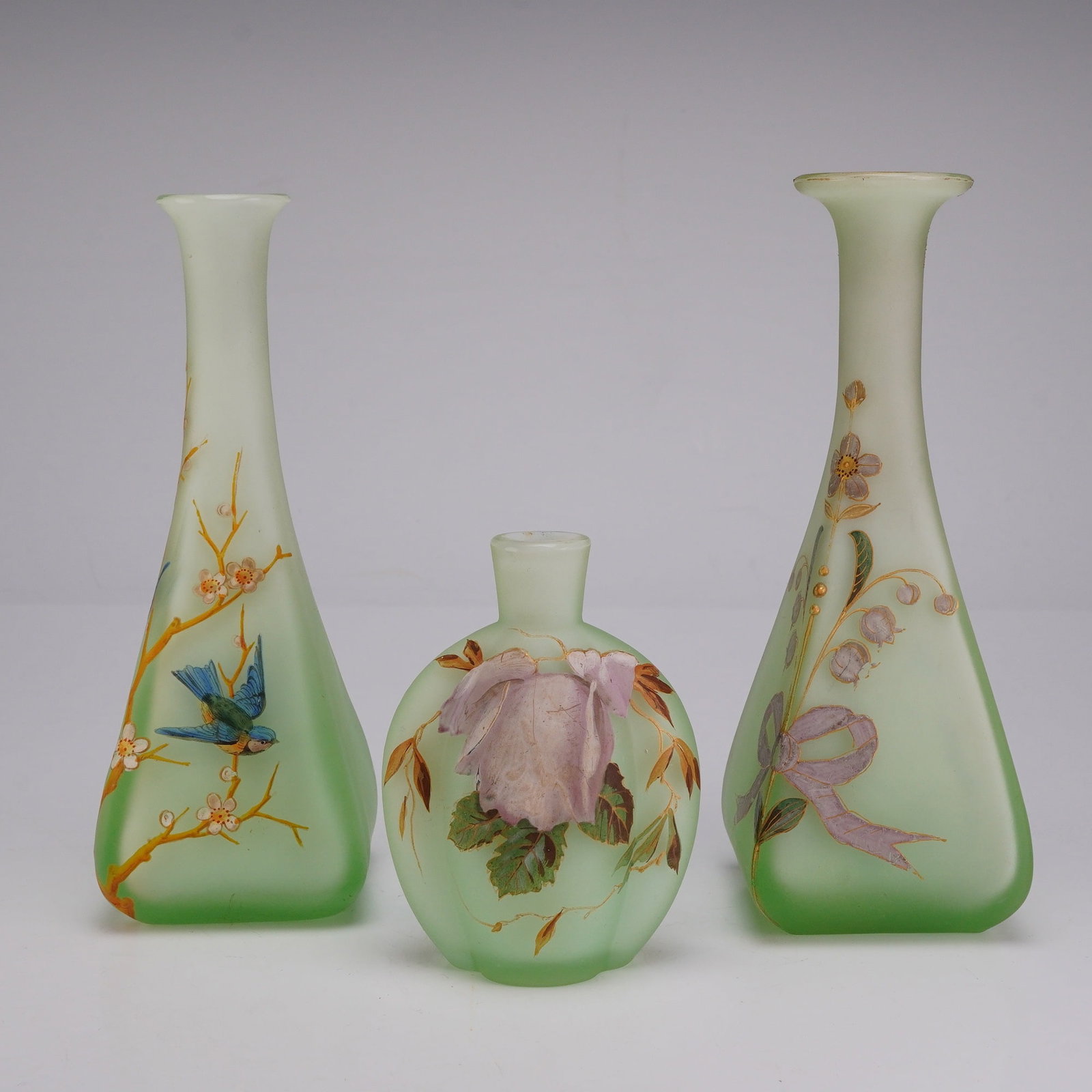 Three Victorian Style Nile Green Satin Glass Vases with Hand Painted Enamel Decoration: This lot features three pieces of glass in the Victorian art glass style, characterized by a uniform pale Nile green color and a frosted satin finish. The group includes two tall tapering bud vases wi