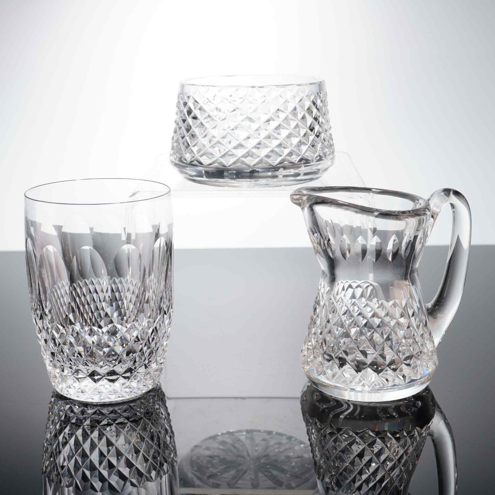 Three Waterford Crystal Items in Alana and Lismore Patterns: This collection of three lead crystal items is manufactured by Waterford. The group includes one straight-sided tumbler, one small creamer, and one small open sugar bowl. The items feature hand-cut de