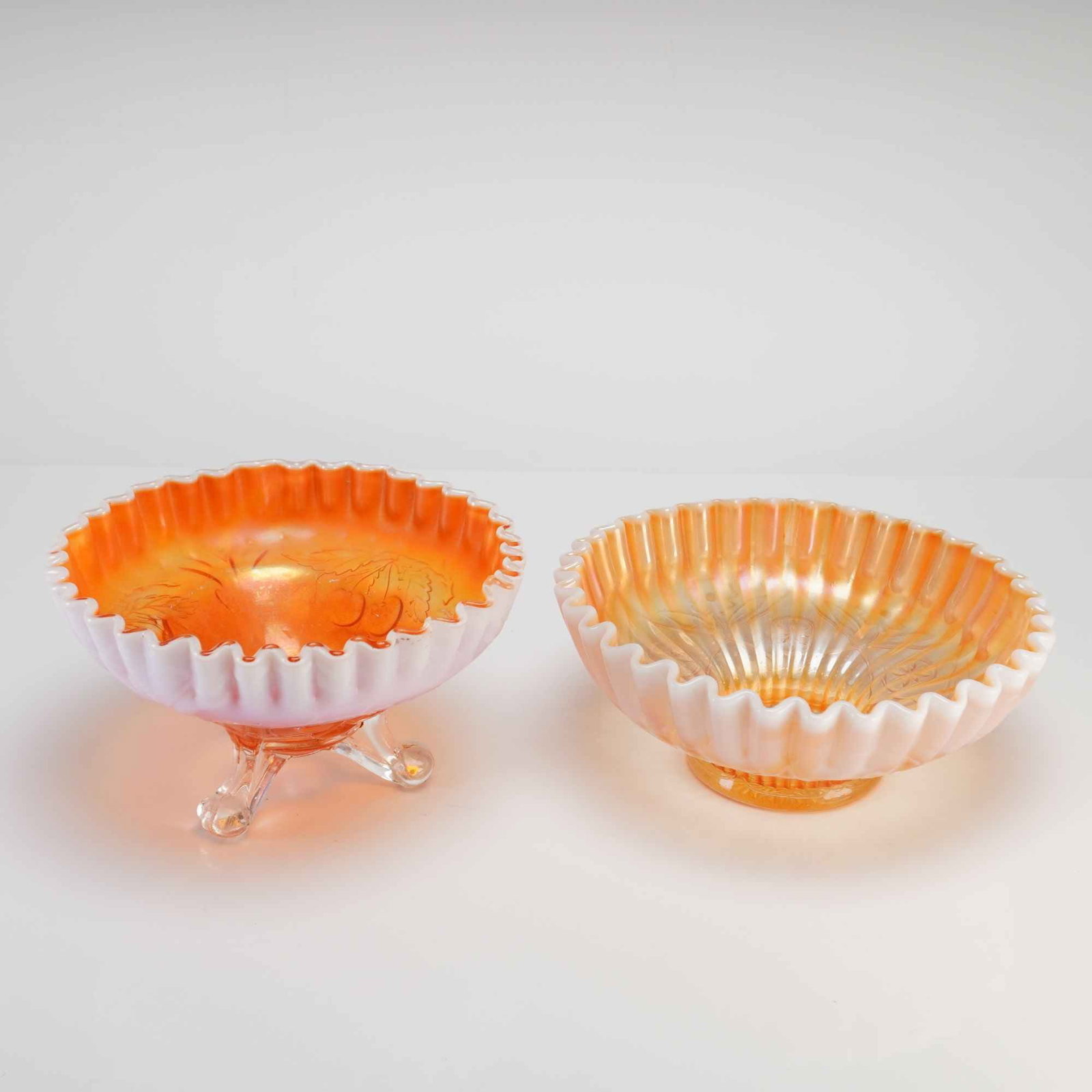 Two American Peach Opalescent Carnival Glass Bowls: This lot features two pieces of American carnival glass in the peach opalescent colorway, characterized by marigold iridescence over a white opalescent base. The first item is a footed bowl in the Che