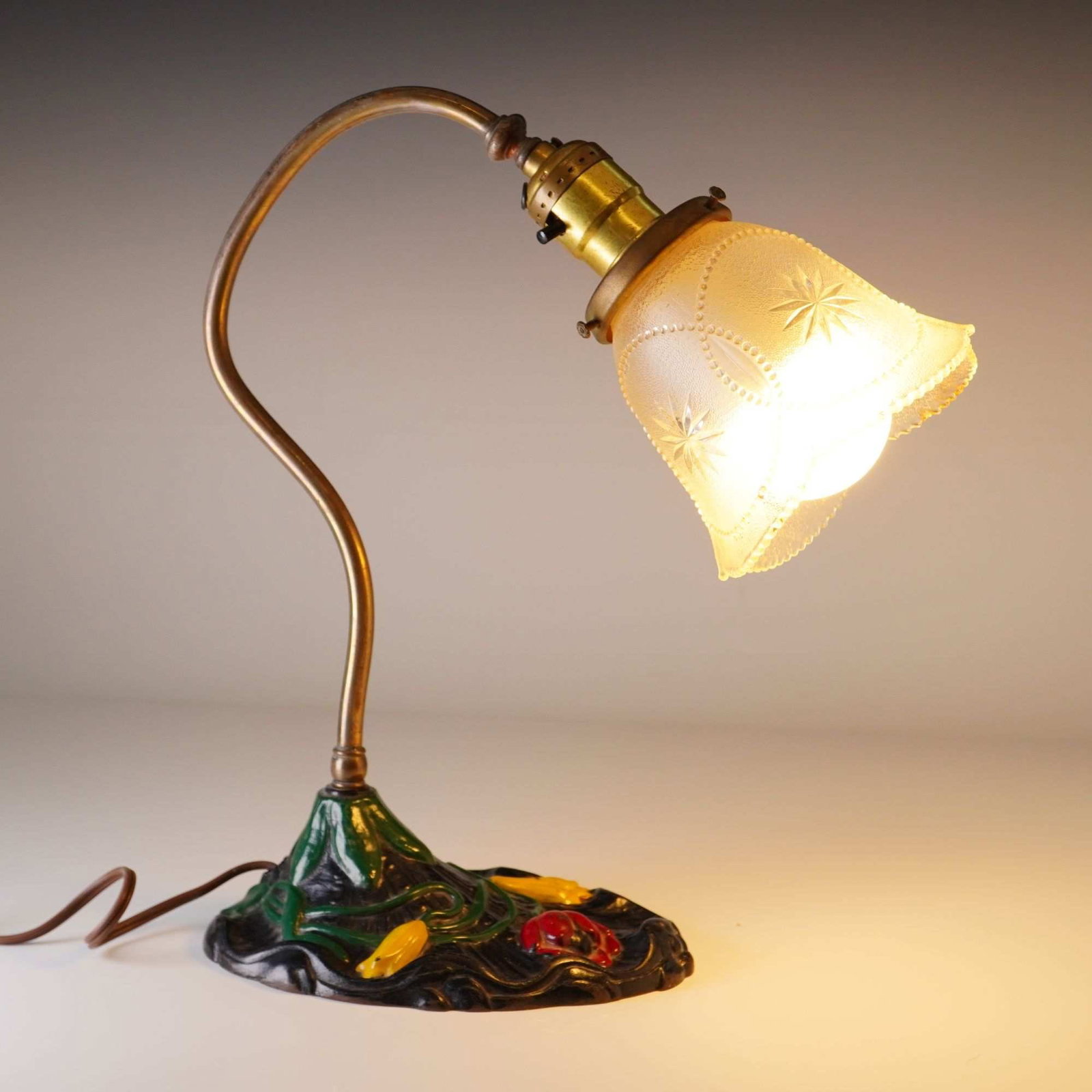 Art Nouveau Revival RMR Metal Casting Cast Iron Desk Lamp w/ Floral Motif & Frosted Glass Shade: This Art Nouveau style desk lamp features a cast iron base with a floral motif, specifically lily pads, finished with polychrome paint in shades of green, red, and yellow. The lamp was produced by