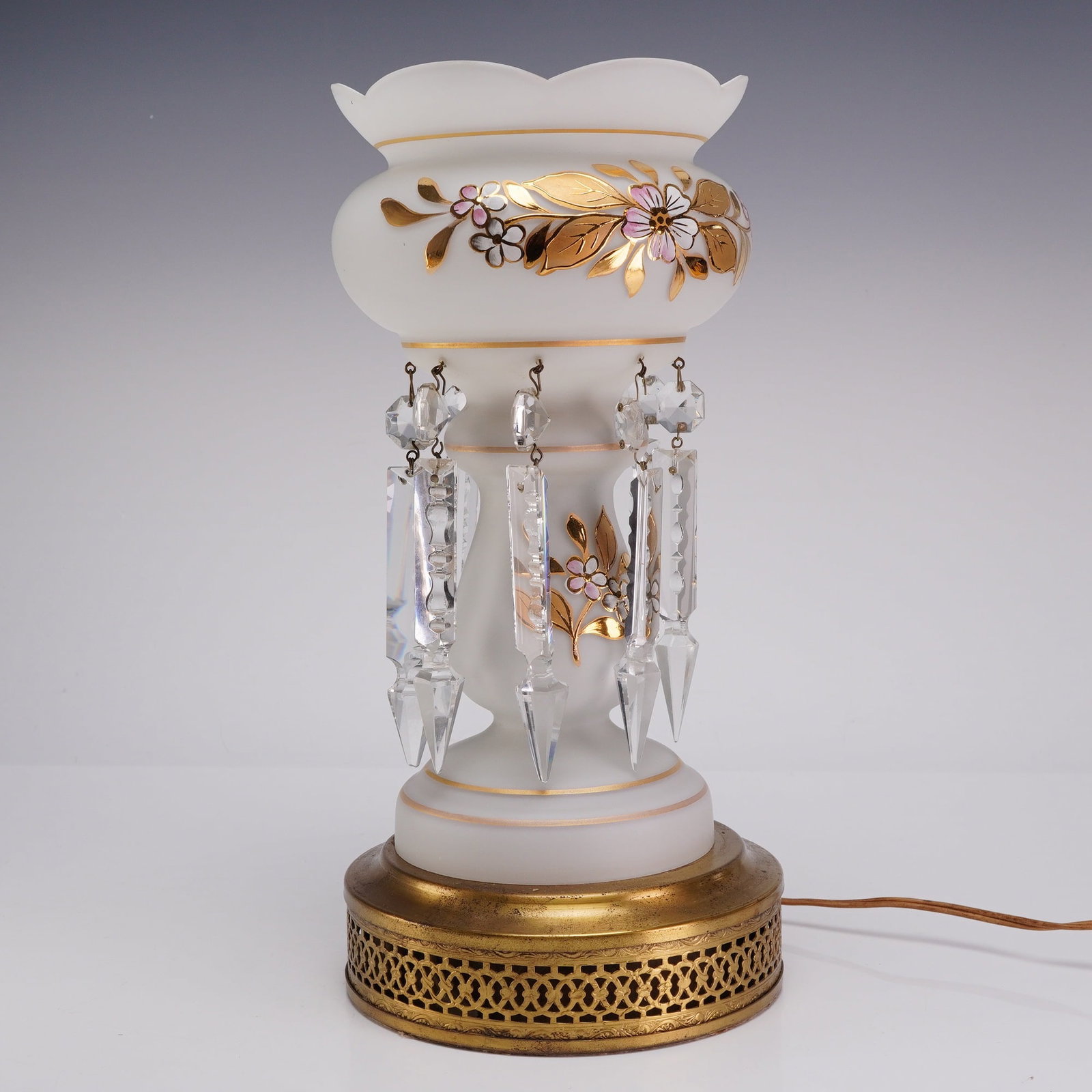 Mid-Century White Satin Glass Mantle Lamp with Hand-Painted Floral Decoration and Crystal Prisms: A mid-century mantle lamp featuring a white satin glass body with a scalloped petal-form rim. The glass is decorated with hand-painted gilt floral motifs and leaves, further accented by pink and