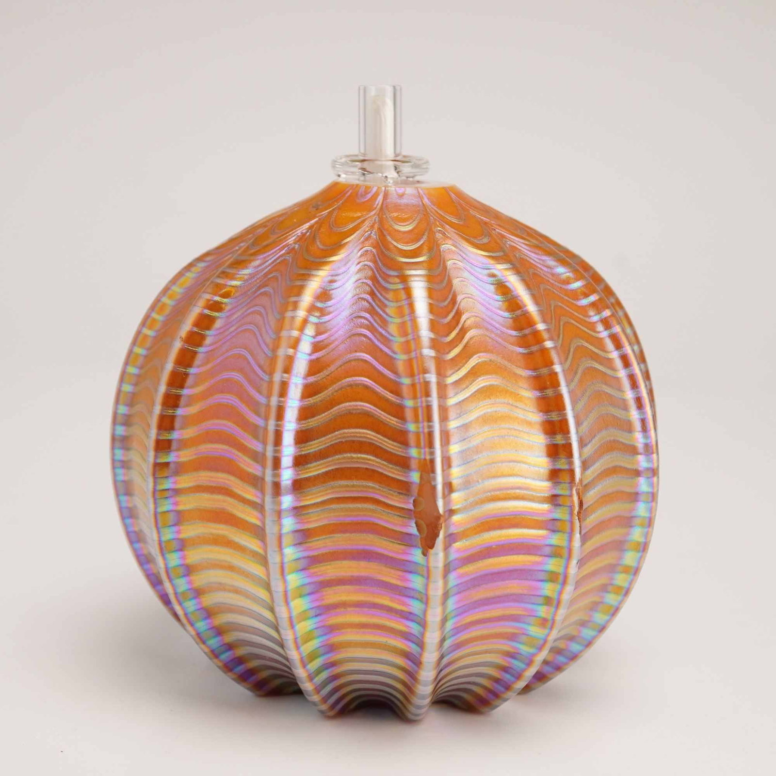 Iridescent Hand Blown Glass Oil Lamp, Signed: An iridescent art glass oil lamp is of globular form with deep vertical ribbing and features an Aurene finish. The exterior is decorated with a continuous horizontal wavy pulled-thread pattern, exhibi