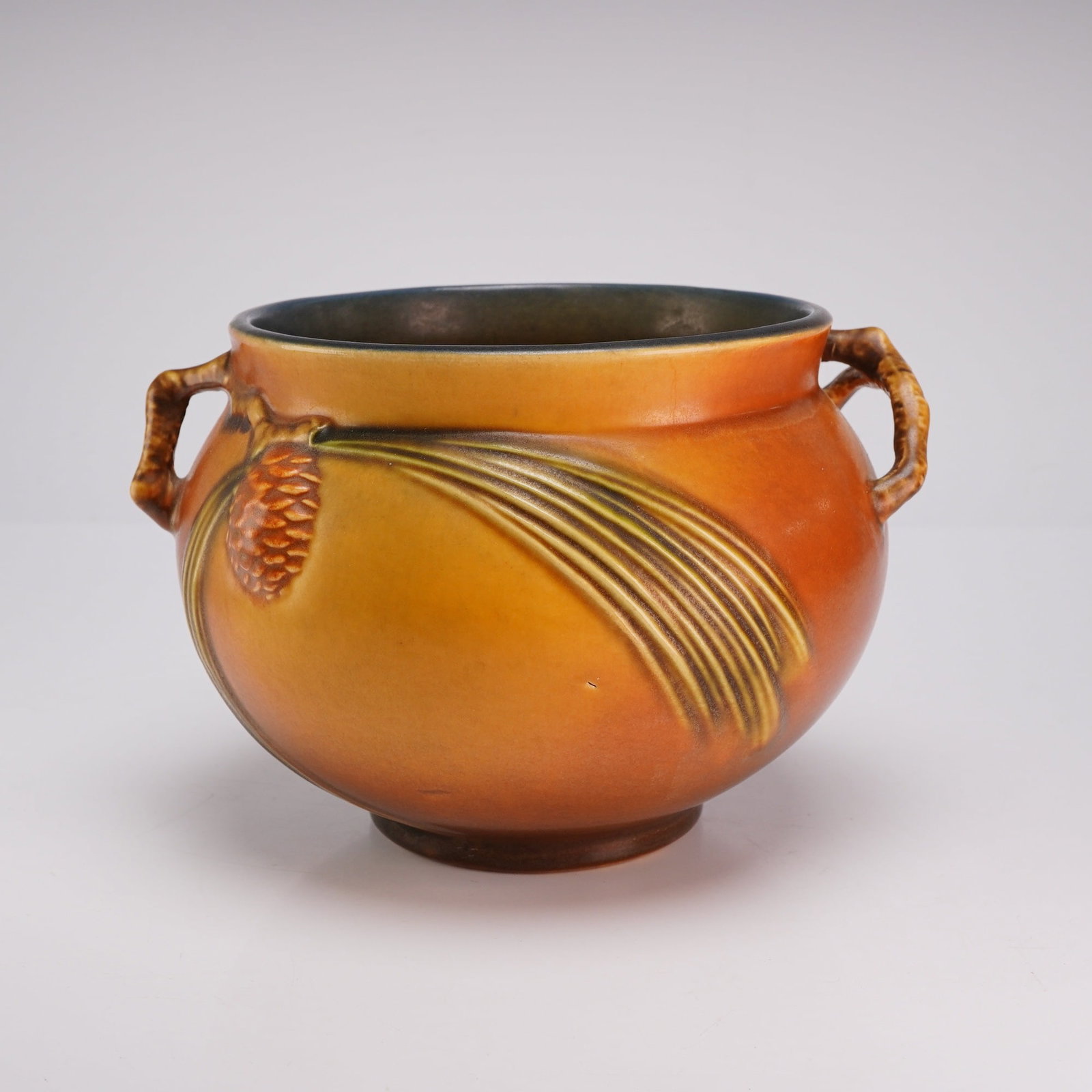 Roseville Pine Cone Brown Art Pottery Handled Jardiniere: A Roseville Pottery Company earthenware jardiniere in the Pine Cone pattern, first introduced in 1935. The vessel features a bulbous body with two small twig-form handles. The exterior is decorated