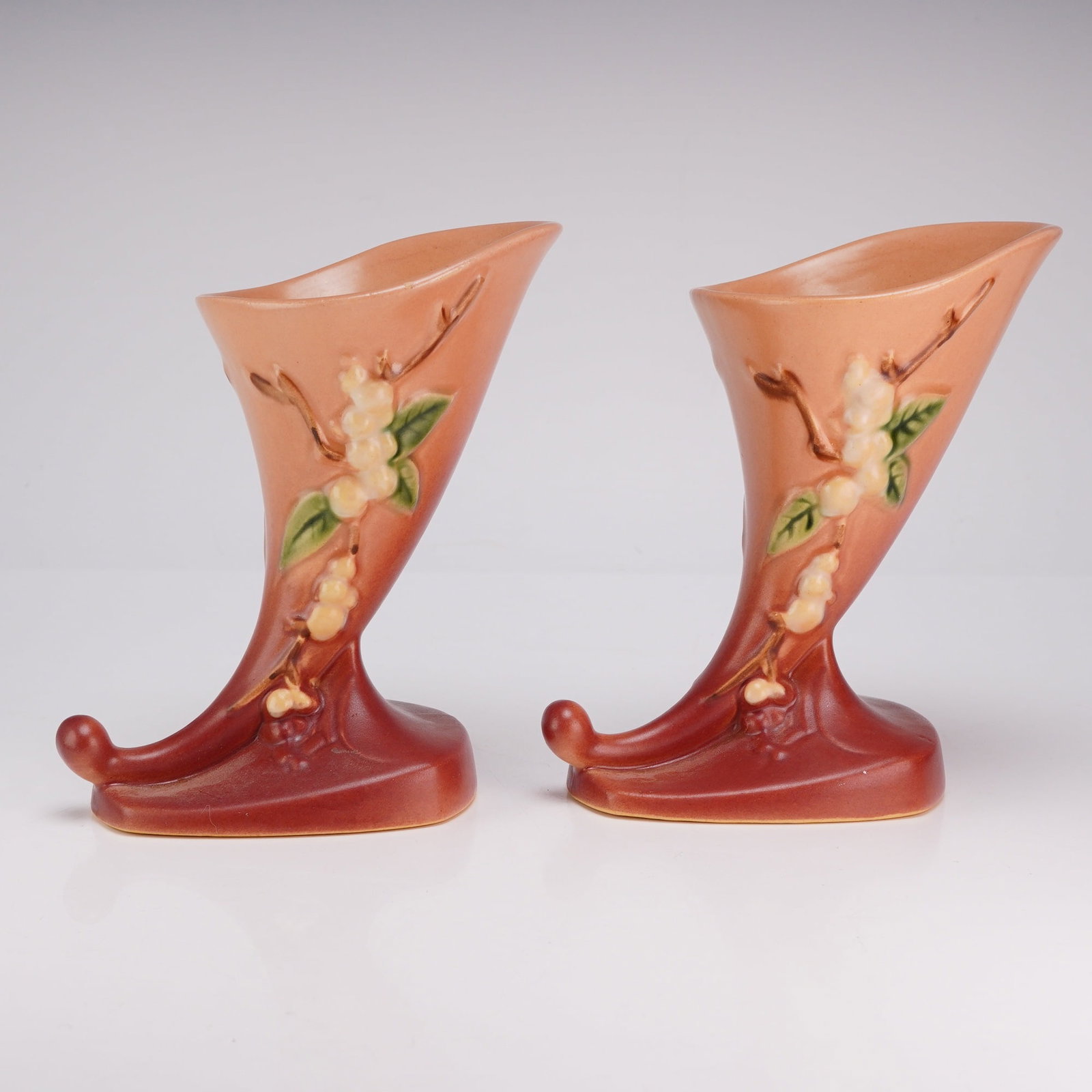 A Pair of Roseville Cornucopia Vases, Snowberry Pink 1CC-6: A pair of Roseville Pottery cornucopia vases in the Snowberry pattern. These earthenware vases feature a matte spray-glazed finish with a chromatic gradient transitioning from a dusky pink at the rim