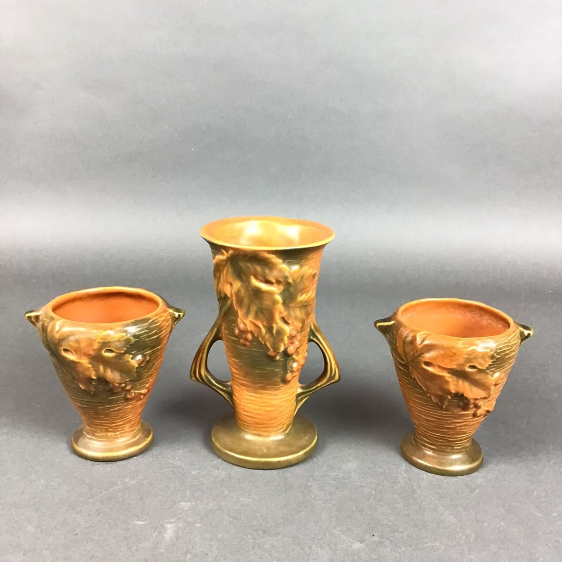 Three Roseville Pottery Vases, Bushberry Brown: This collection of American art pottery was manufactured by Roseville Pottery in the Bushberry pattern, first introduced circa 1941. The earthenware set features a matte glaze in the Russet colorway,