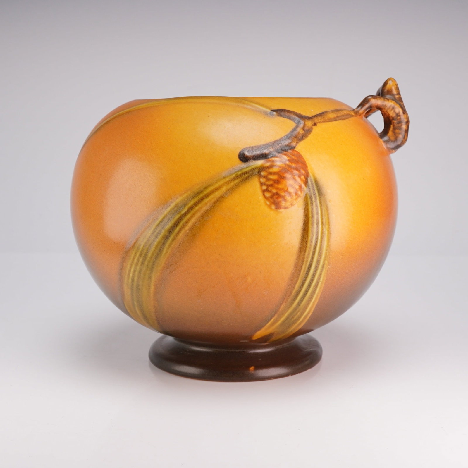 Roseville Pottery Ball Vase, Pinecone 261-6: This earthenware vessel features a globular form with a matte glaze in a graded amber and brown colorway. The piece is decorated with molded relief pinecones and needles on both sides, complemented