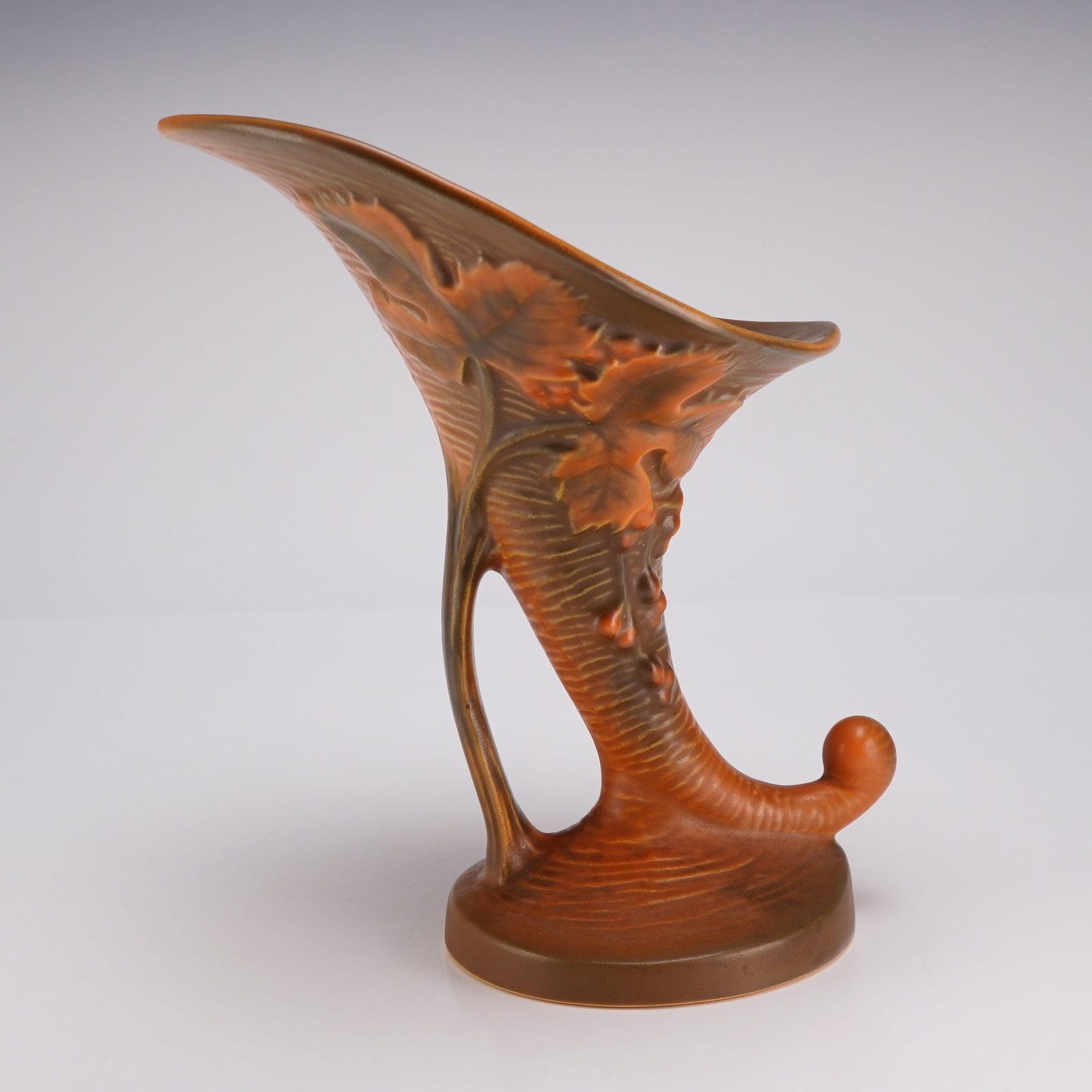 Roseville Pottery Cornucopia Vase, Bushberry Brown 154-8: This earthenware art pottery piece features a wide, scalloped rim and a tapering, curved body terminating in a scrolled, ball-shaped tip. The body is supported by a circular, tiered base and a