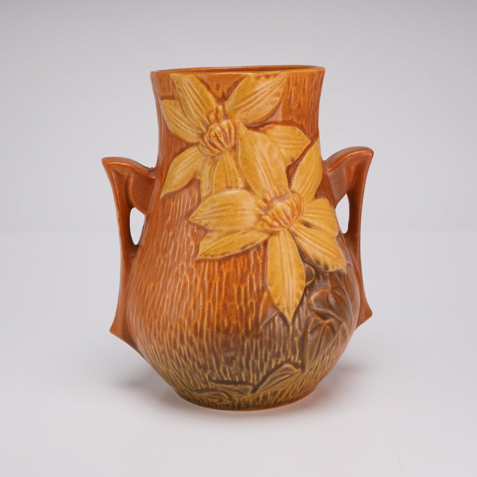 Roseville Pottery Double Handled Vase, Clematis Brown 103-6: This earthenware art pottery vase was produced by Roseville Pottery in Zanesville, Ohio, as part of the Clematis pattern originally introduced circa 1945. The piece features relief-molded floral