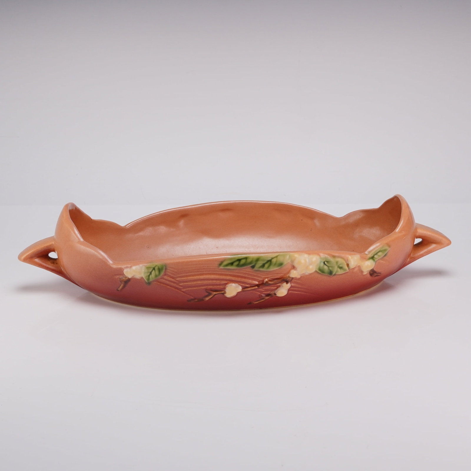 Roseville Pottery Snowberry Pink Console Bowl: Roseville Pottery Snowberry pattern art pottery console bowl. This earthenware vessel, introduced in 1947, features an elongated, shallow form with a wavy rim and two integral, pointed handles. The ex