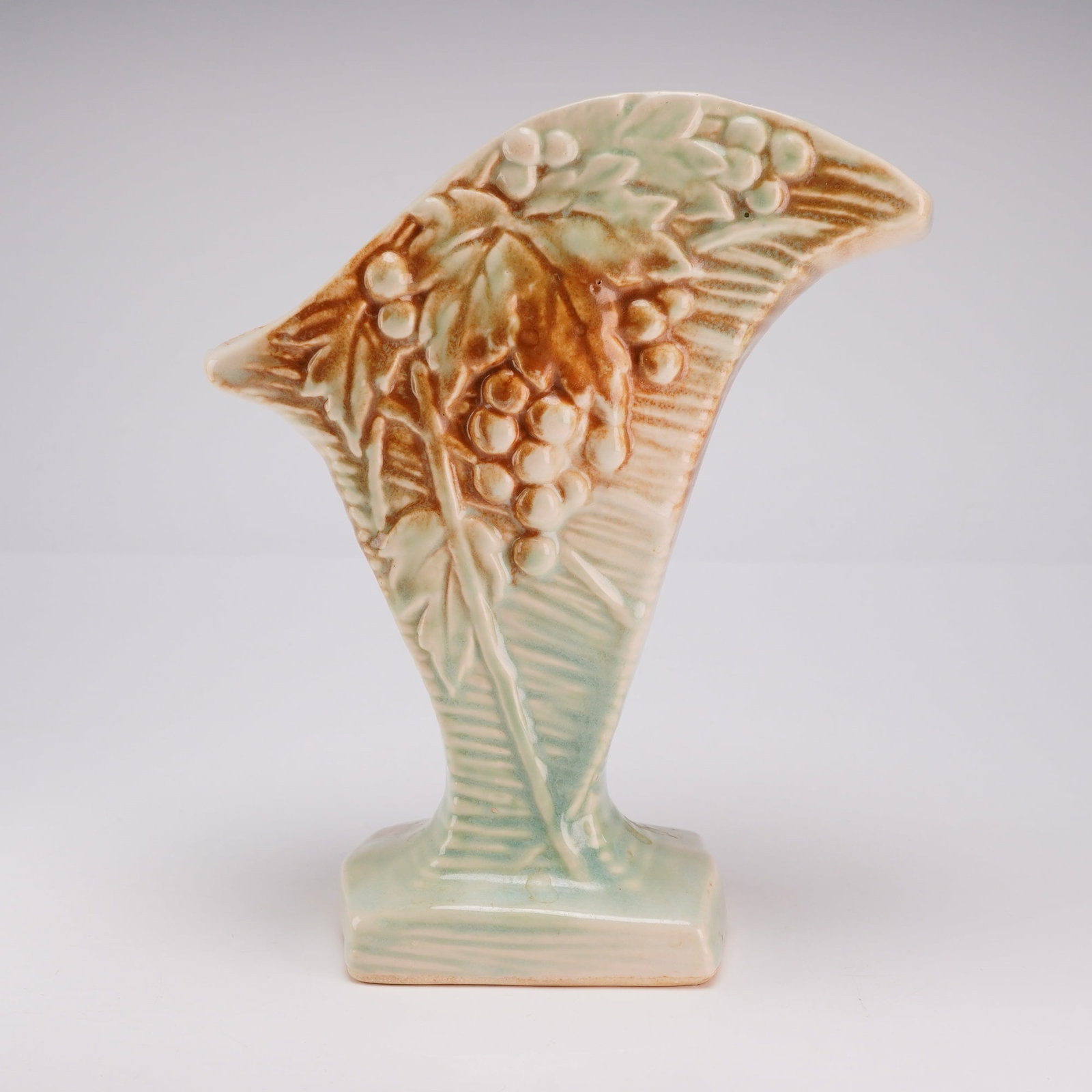 McCoy Pottery Grapevine Fan Vase, Rustic Line: This American art pottery fan vase, attributed to McCoy, features a relief-molded grapevine motif. The vessel is constructed in a stylized wing or fan form that tapers to a rectangular pedestal base. 