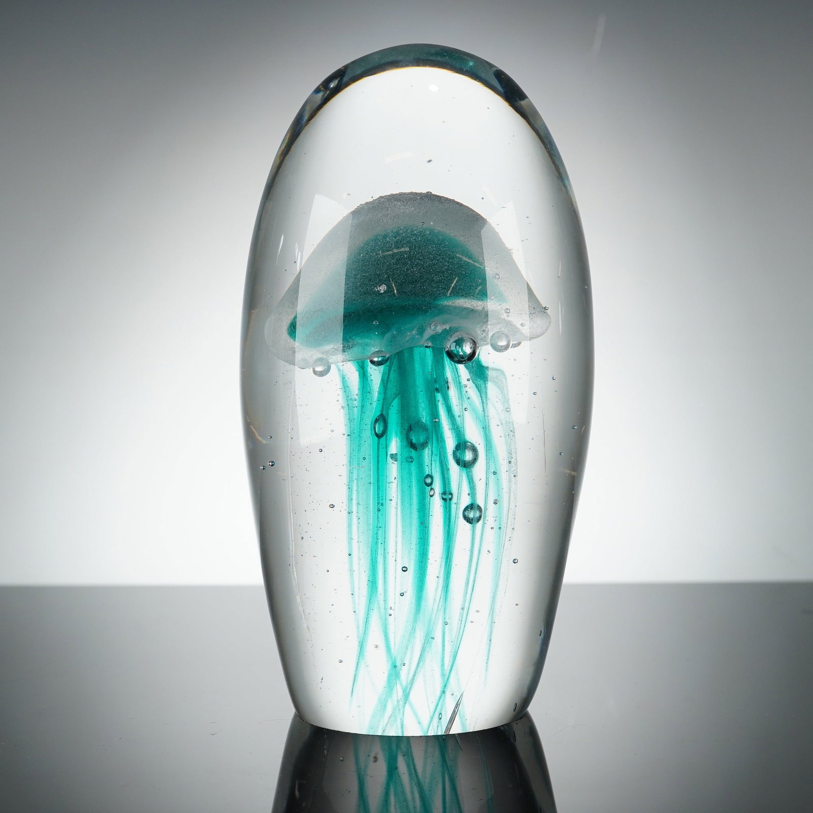 Dynasty Gallery Art Glass Jellyfish Themed Paperweight: This art glass jellyfish themed paperweight is produced by Dynasty Gallery. The piece is constructed of solid clear glass in an ovoid form, featuring an encased lampwork jellyfish motif in shades of t