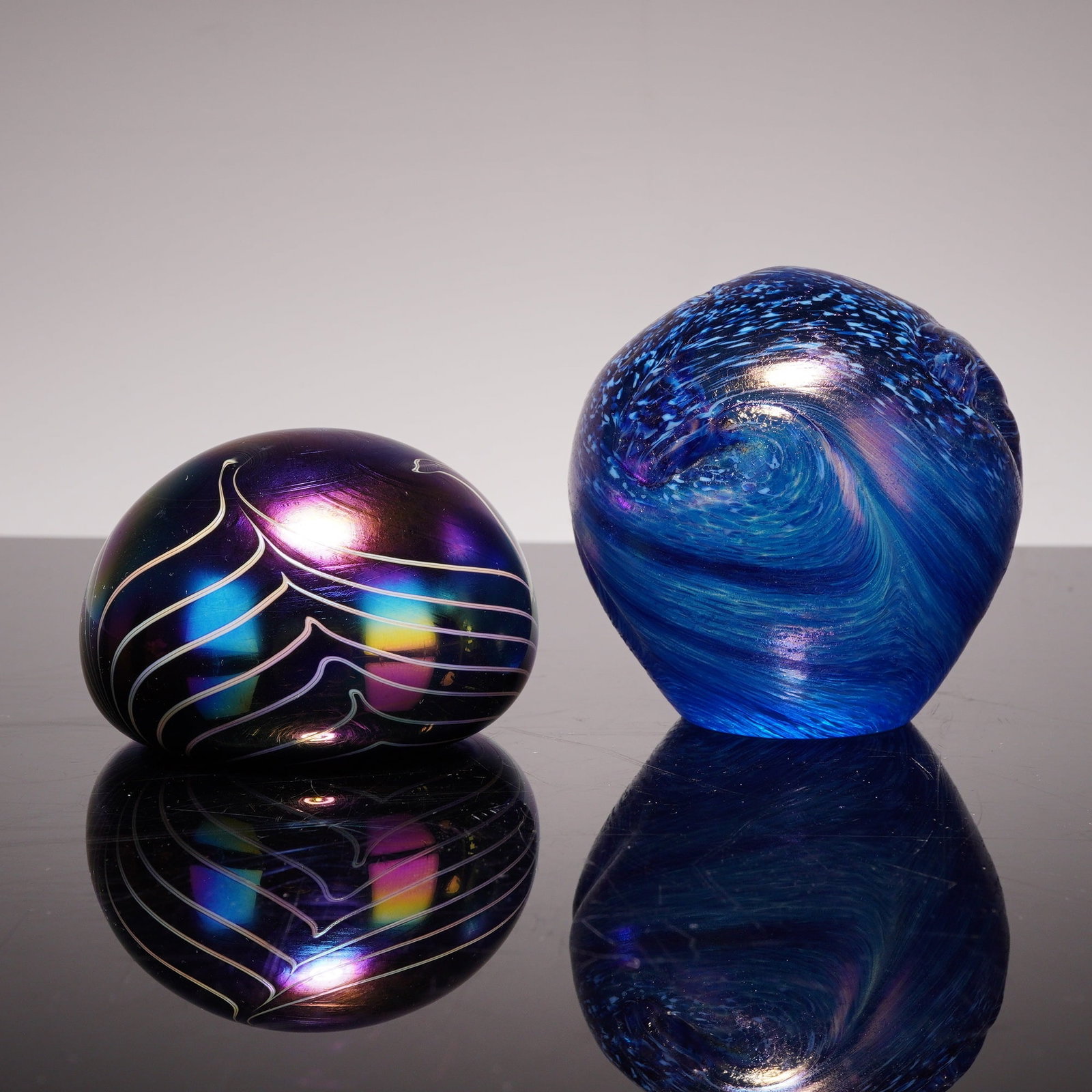 Two Contemporary Iridescent Studio Art Glass Paperweights: Two contemporary studio art glass paperweights with iridescent finishes. The collection includes a surface-decorated iridescent pulled-feather paperweight in the style of Terry Crider. This piece is o