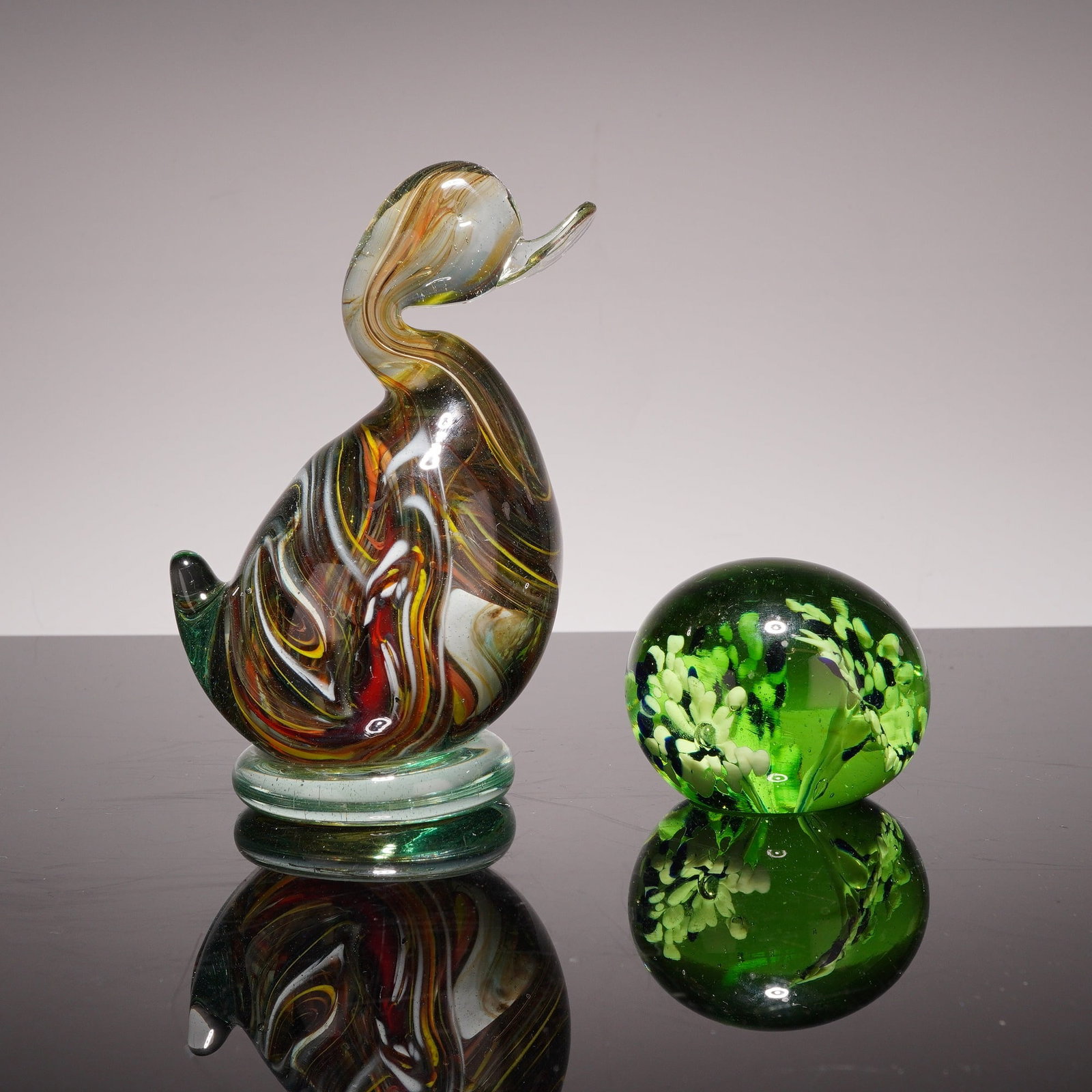 Two Pieces of Art Glass - Murano Style Duck Figurine and Floral Paperweight: The first item is a duck shaped figurine featuring internal swirls in gold and brown tones, with additional accents of black, white, and red. The figurine is constructed with a curved neck and a clear