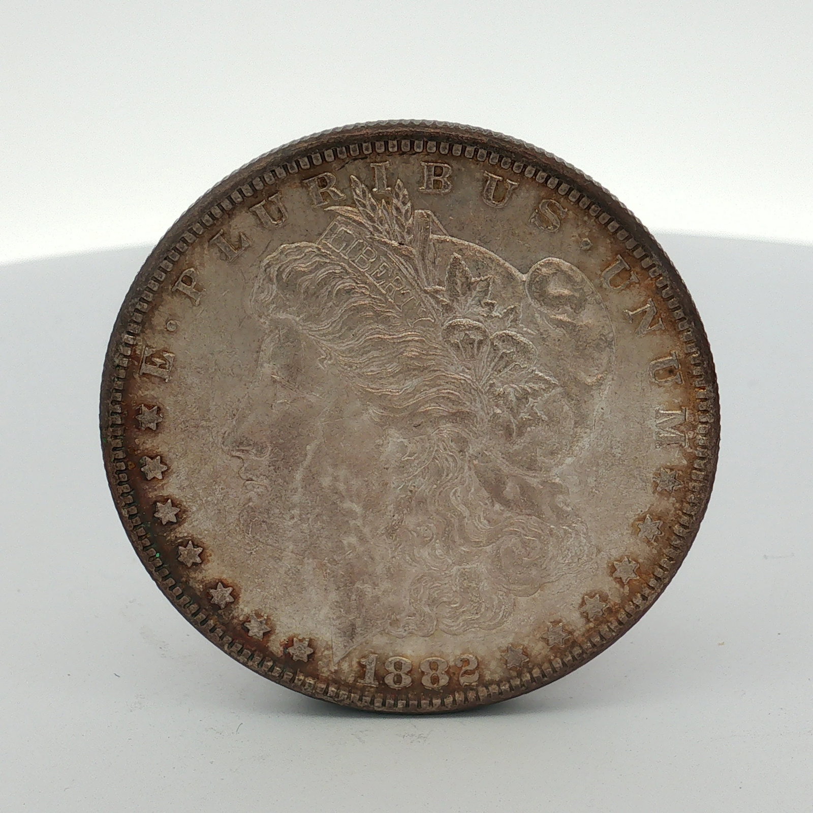 1882 US One Dollar Morgan Silver Dollar, Circulated: This 1882 US Morgan dollar was struck at the Philadelphia Mint. The coin is composed of 0.900 fine silver. It features the Liberty head obverse and the heraldic eagle reverse. Inscriptions include E P