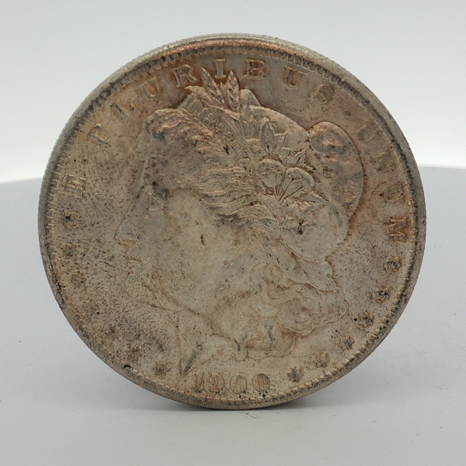 US 1900-O Morgan Silver Dollar: This US 1900 Morgan dollar is a silver coin struck at the New Orleans Mint. The piece features the Morgan dollar design on both the obverse and reverse. The edge is reeded. Inscriptions include the da