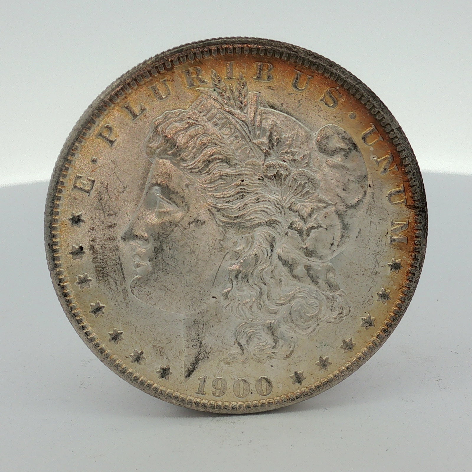 US 1900-O Morgan Silver Dollar: This US silver coin is a 1900 Morgan dollar struck at the New Orleans Mint. The obverse features the Liberty head design with the date 1900 and the inscription E PLURIBUS UNUM. The reverse displays th