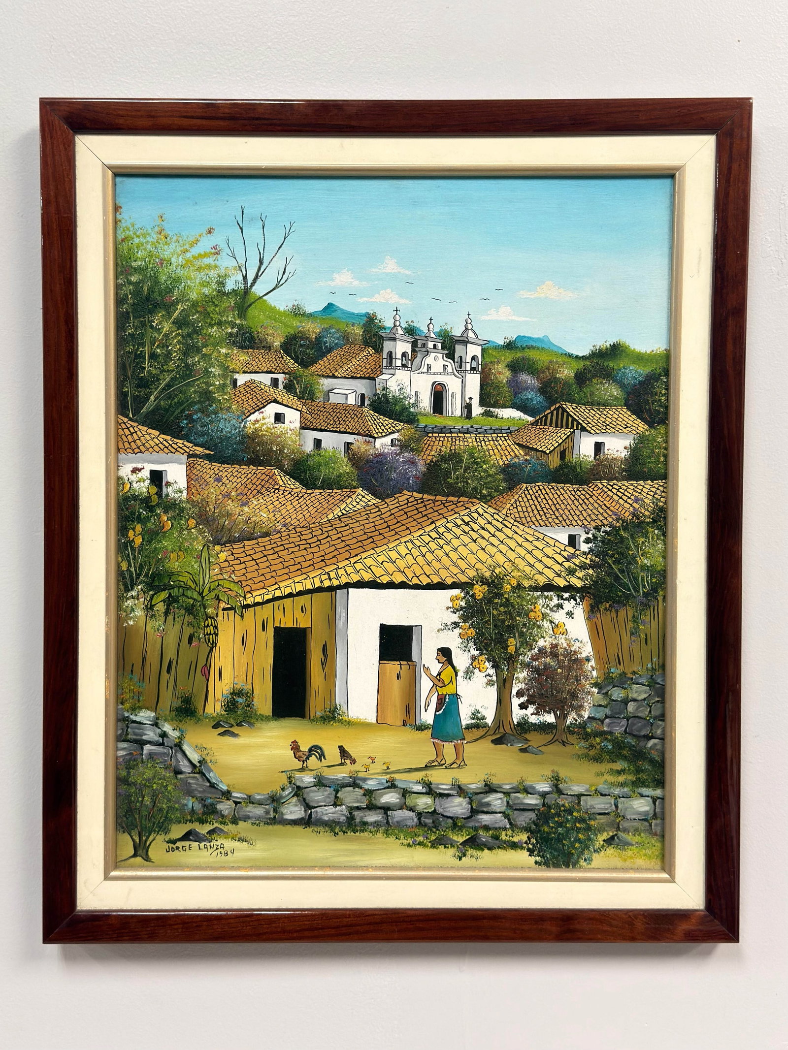Jorge Lanza (Honduran, 20th Century), Village Landscape, 1984, Oil on Canvas: This village landscape is an oil on canvas painting by the Honduran artist Jorge Lanza. Created in 1984, the work is executed in a naive style, portraying a hillside town with numerous white-walled bu