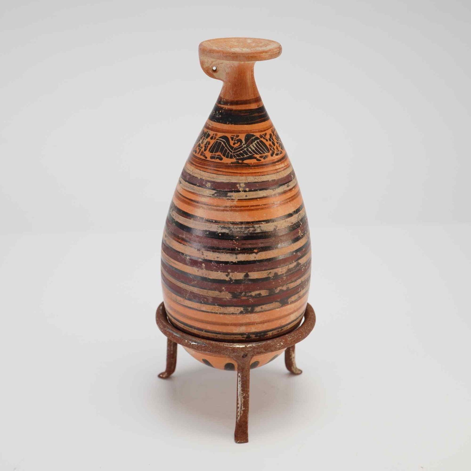 Ancient Greek Corinthian Alabastro Vessel, with Metal Stand: An ancient Greek Corinthian alabastron decorated with a striped pattern and an animal frieze in various shades of brown, accompanied by a metal stand. Dimensions 3"W x 7"H Weight 8.0 oz