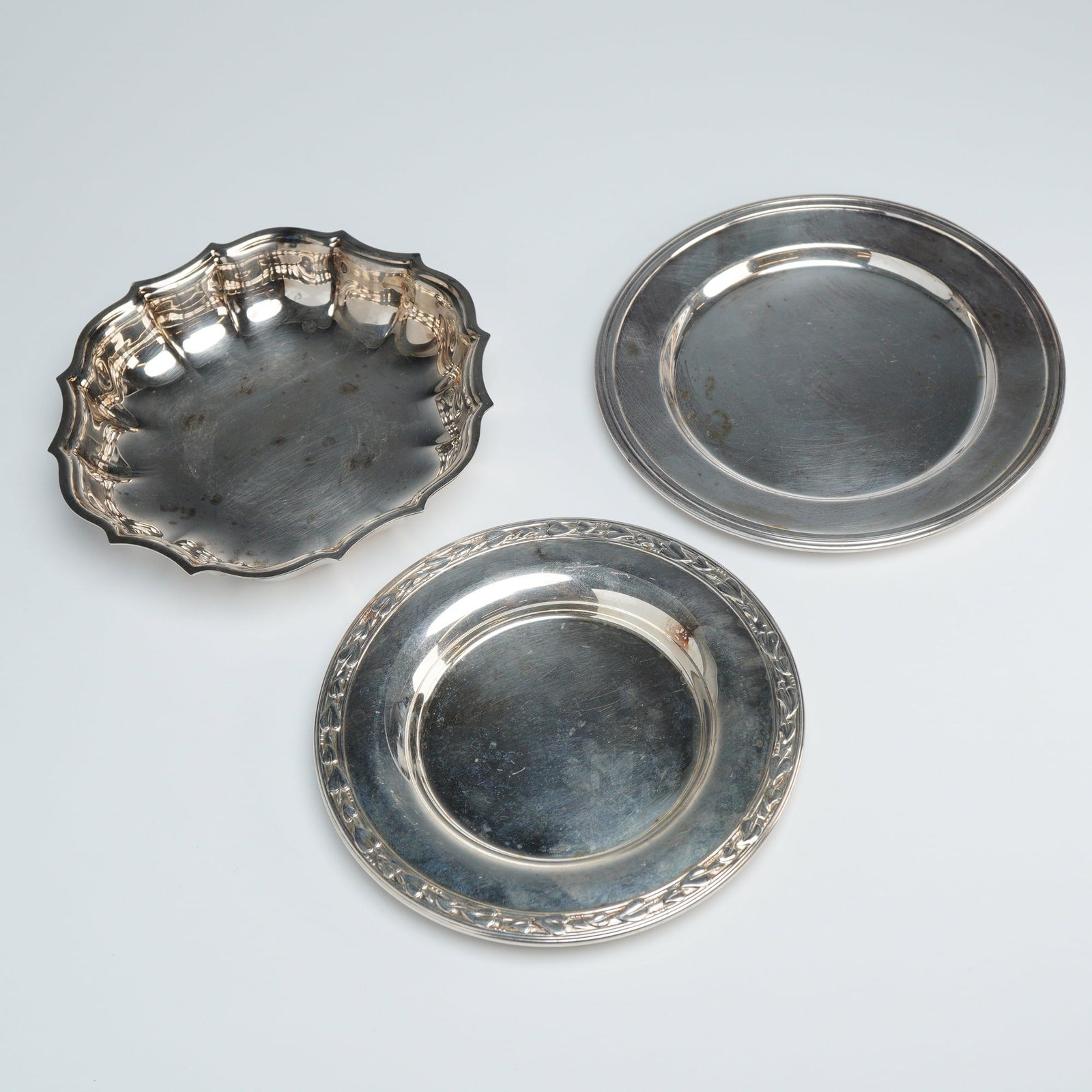 3pc International Silver, Wm. A. Rogers, & Concord Silverplated Dishes: The group includes two circular plates and one scalloped bowl. One plate features a classic plain rim with the name CONCORD engraved on the underside. The second plate is decorated with an embossed fo