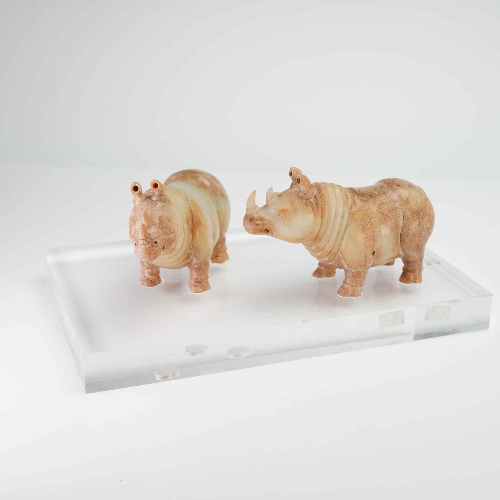 Pair of Ming Dynasty White Nephrite Jade Rhinos: A pair of Chinese finely carved jade rhinoceros figures with base, executed in an archaic style. The figures are carved from white nephrite jade, with a coloration ranging from cream to brown. Each fi