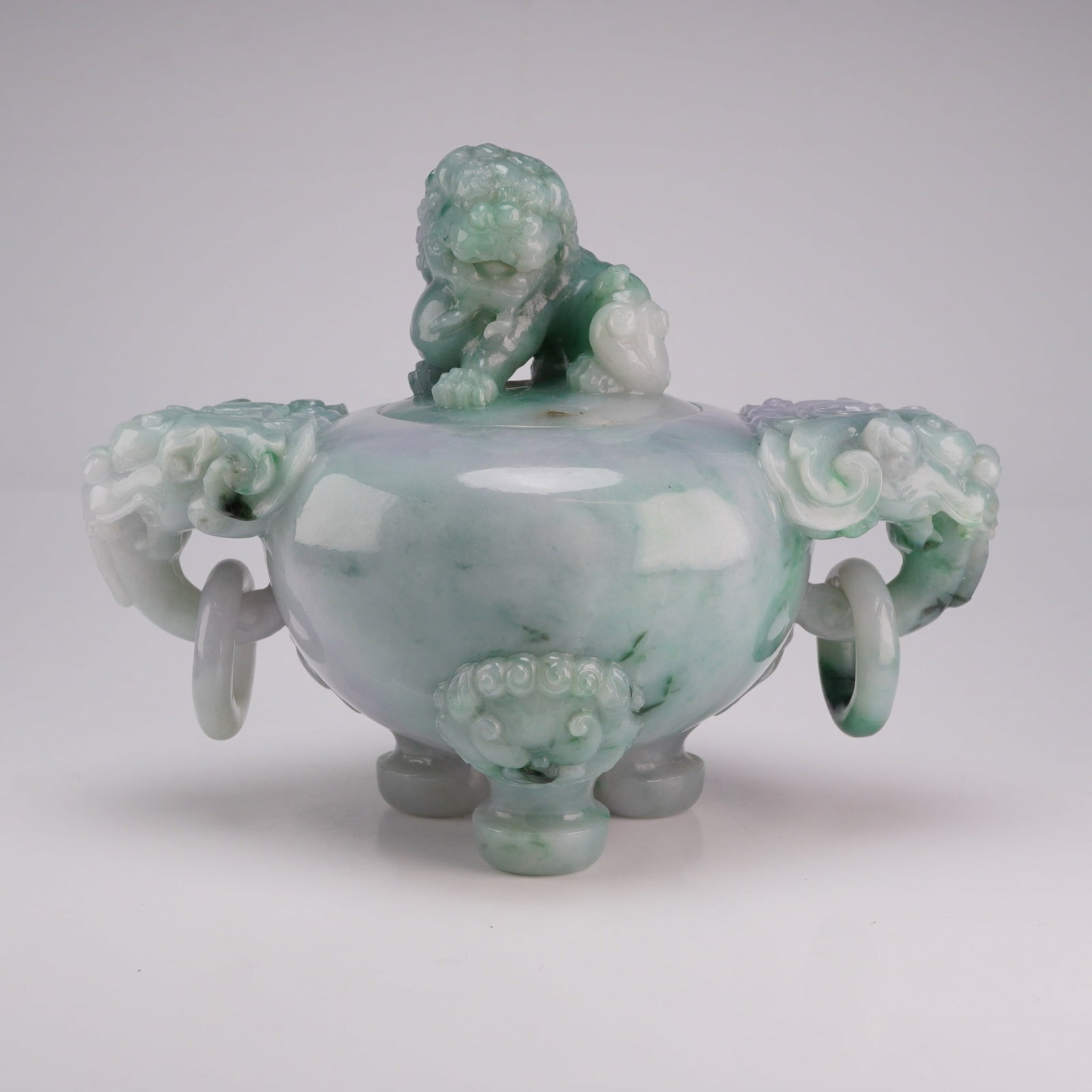 Jadeite Tripod Censer, Buddhist Lion Finial and Handles: This tripod jadeite censer with a lid features hues ranging from bluish-white to green. It has a lion finial on the lid and lion head handles with rings hanging from them. Dimensions 6"L x 3.5"W x 4.5