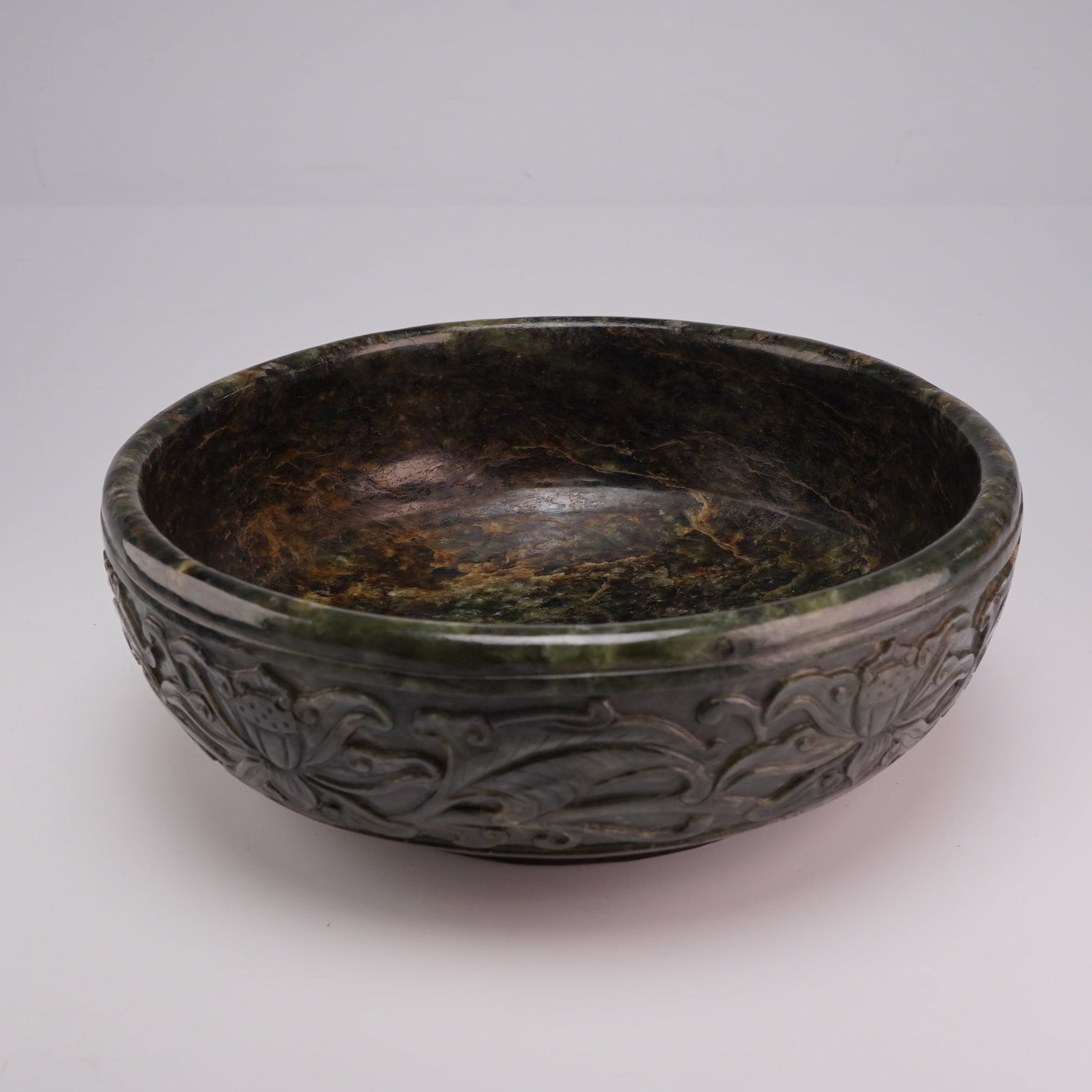 Chinese Spinach Jade Bowl, Lotus Design, Incised Qianlong Mark: A Chinese decorative bowl carved from spinach jade, featuring a lotus design on the exterior. The base is incised with a Qianlong mark. Dimensions 2"H x 6.5" dia. Weight 1.110 lb