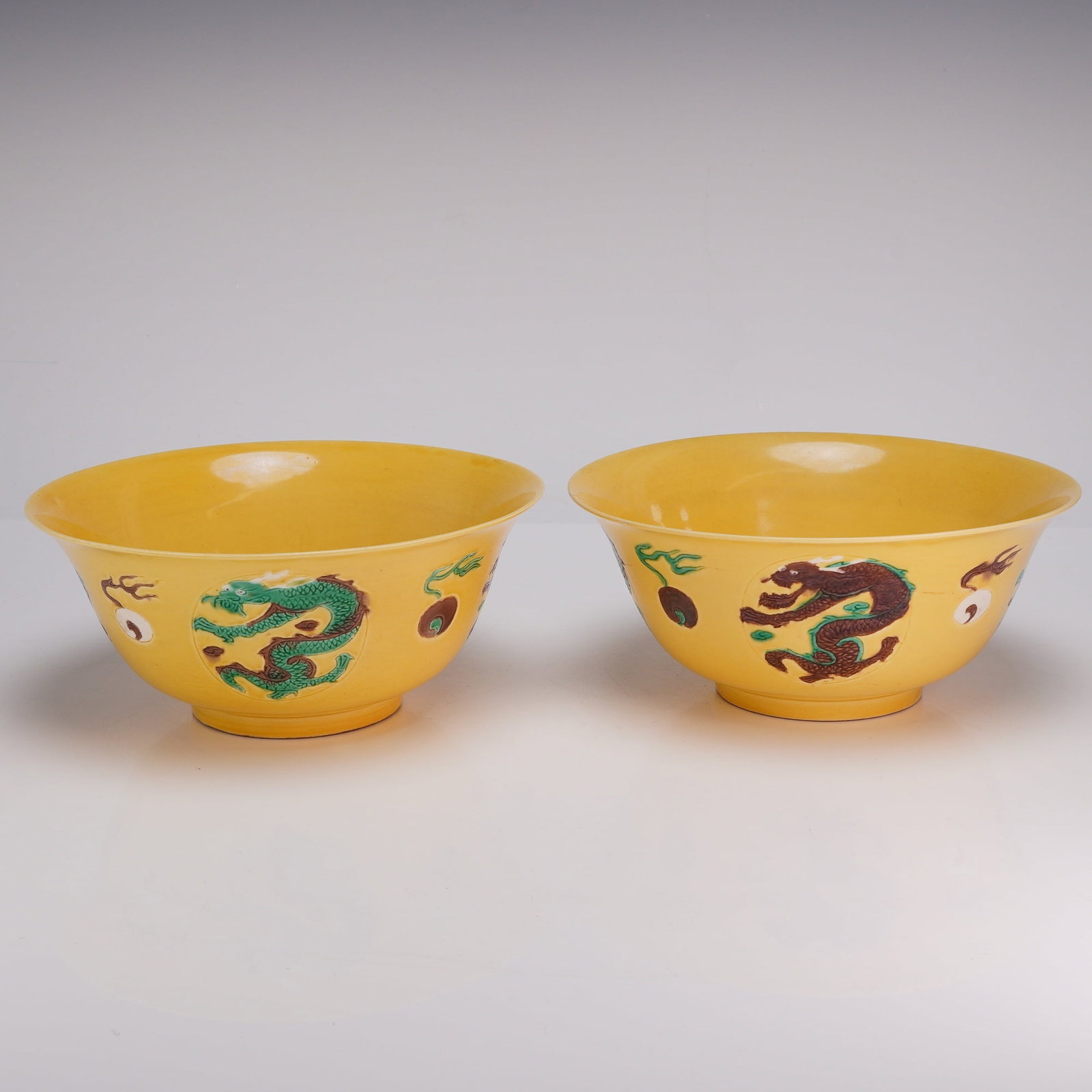 Pair of Yellow Glaze Bowls, Kangxi Mark, Dragons and Flaming Pearls: A pair of yellow glazed bowls decorated with dragons and flaming pearls in shades of brown, green, and white. Each bears Kangxi marks on the underside. Dimensions Each: 7.75"W x 3.5"H Weight 2.80 lbs