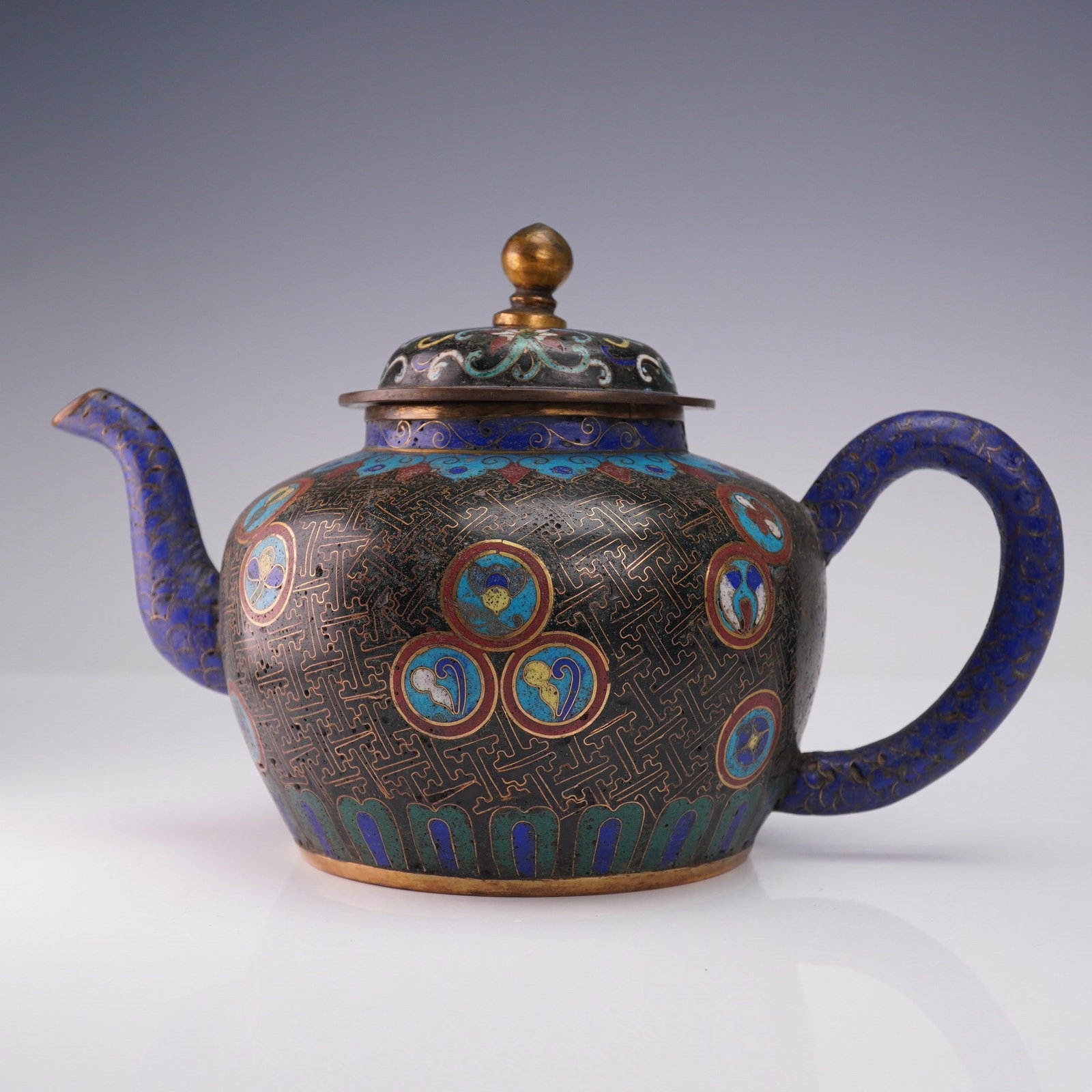 2pc Cloisonne-Enamel Teapot and Lid: The teapot features a globular body with a loop handle positioned opposite an S-curved spout. The body is decorated with polychrome roundels, each enclosing a blossom, set against a black diaper-patte