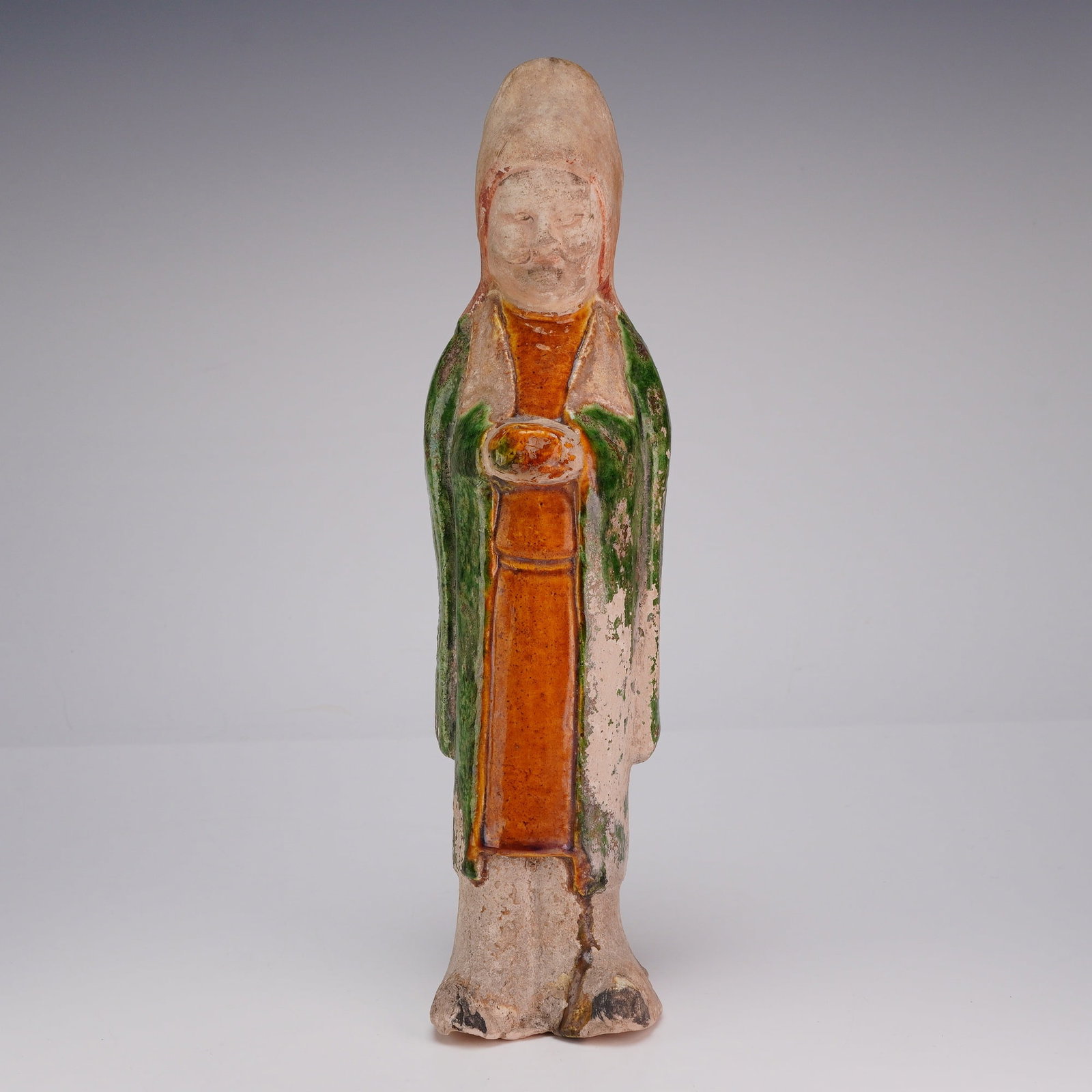 Chinese Sancai Glazed Standing Figure, Attendant, Tang Dynasty: A Chinese Sancai glazed figure of an attendant wearing an orange dress and a green robe. Dimensions 2.5"L x 2.5"W x 9.5"H Weight 13.0 oz