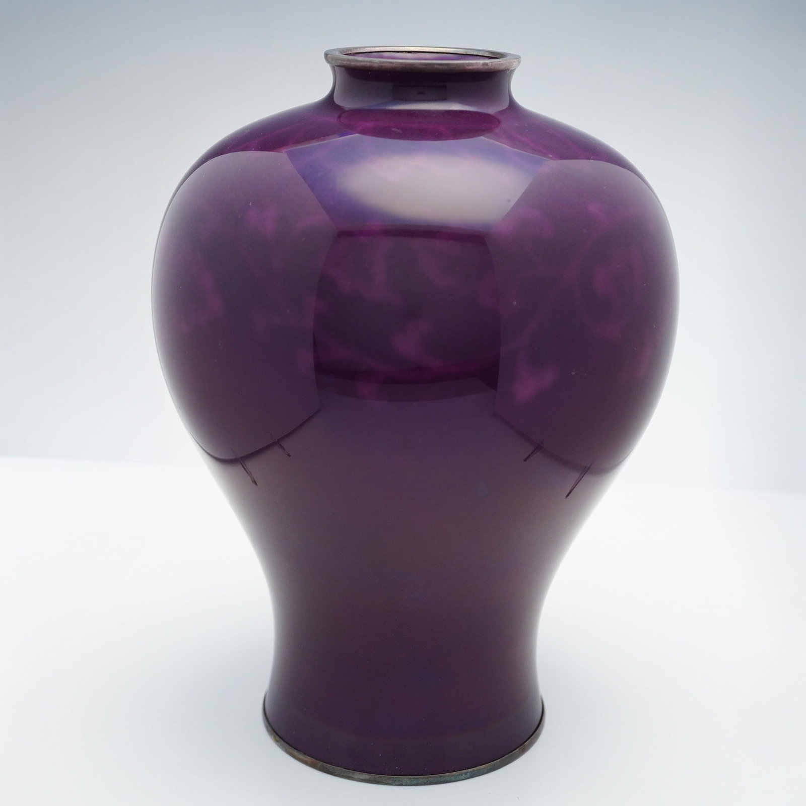 Japanese Wireless Cloisonne Vase, Ando, Silver Rims: A Japanese wireless cloisonne vase finished in a plum purple glaze, decorated with a faint vine and leaf pattern around the body and a floral-like pattern around the rim. The rim and base are trimmed 