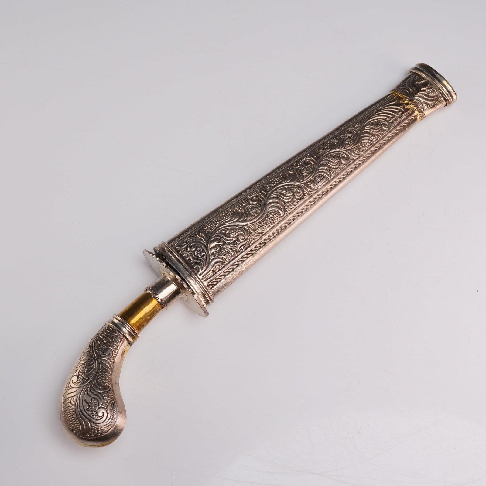 Moro Gunong Dagger and Sheath: A Moro gunong dagger, an Islamic style knife traditional to the Southern Philippines. The dagger features a wavy-edged steel blade with a flared base. The pistol-grip hilt is decorated with chased