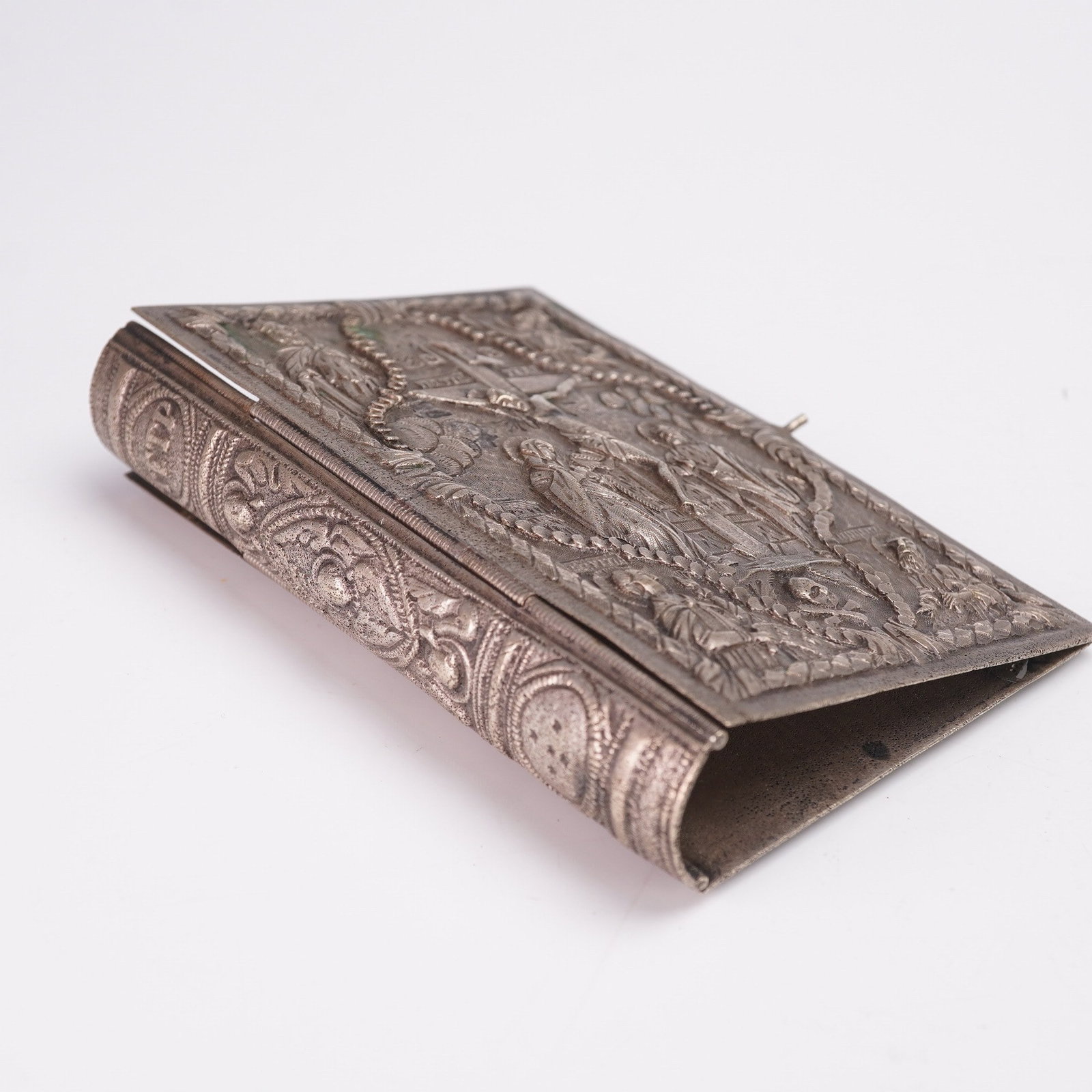 Cast Silver Religious Repousse Bible Book Cover: Cast silver religious repousse Bible cover. The hinged cover features intricate relief scenes depicting significant Christian iconography. The front side depicts the Crucifixion, flanked by additional