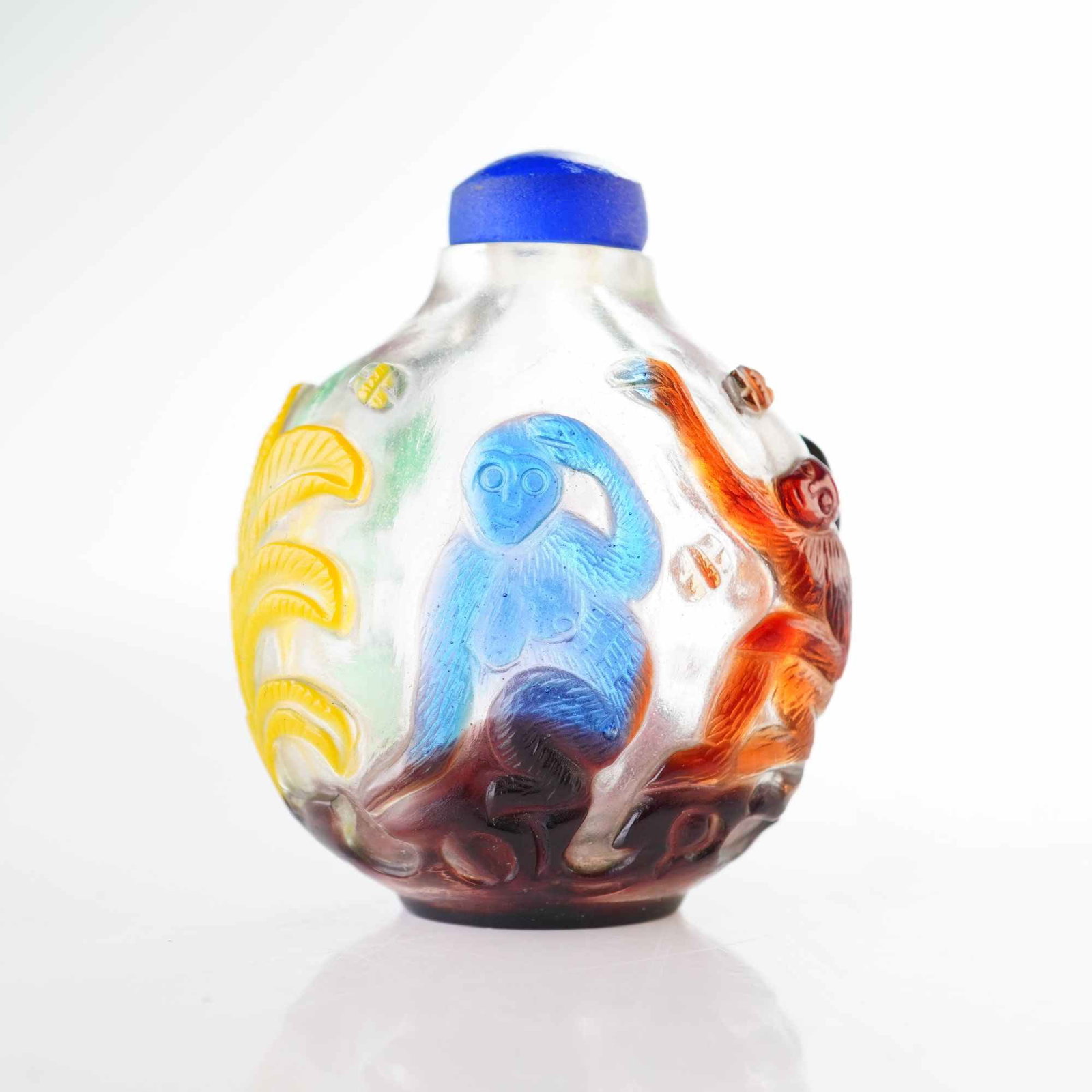 Peking Glass Snuff Bottle, Multi-color Overlay Monkeys: This clear Peking glass bottle features a round form and is decorated with multi-color relief overlay depicting monkeys and botanical elements. Presented with a blue stopper. Dimensions 1.75"L x 1"W x