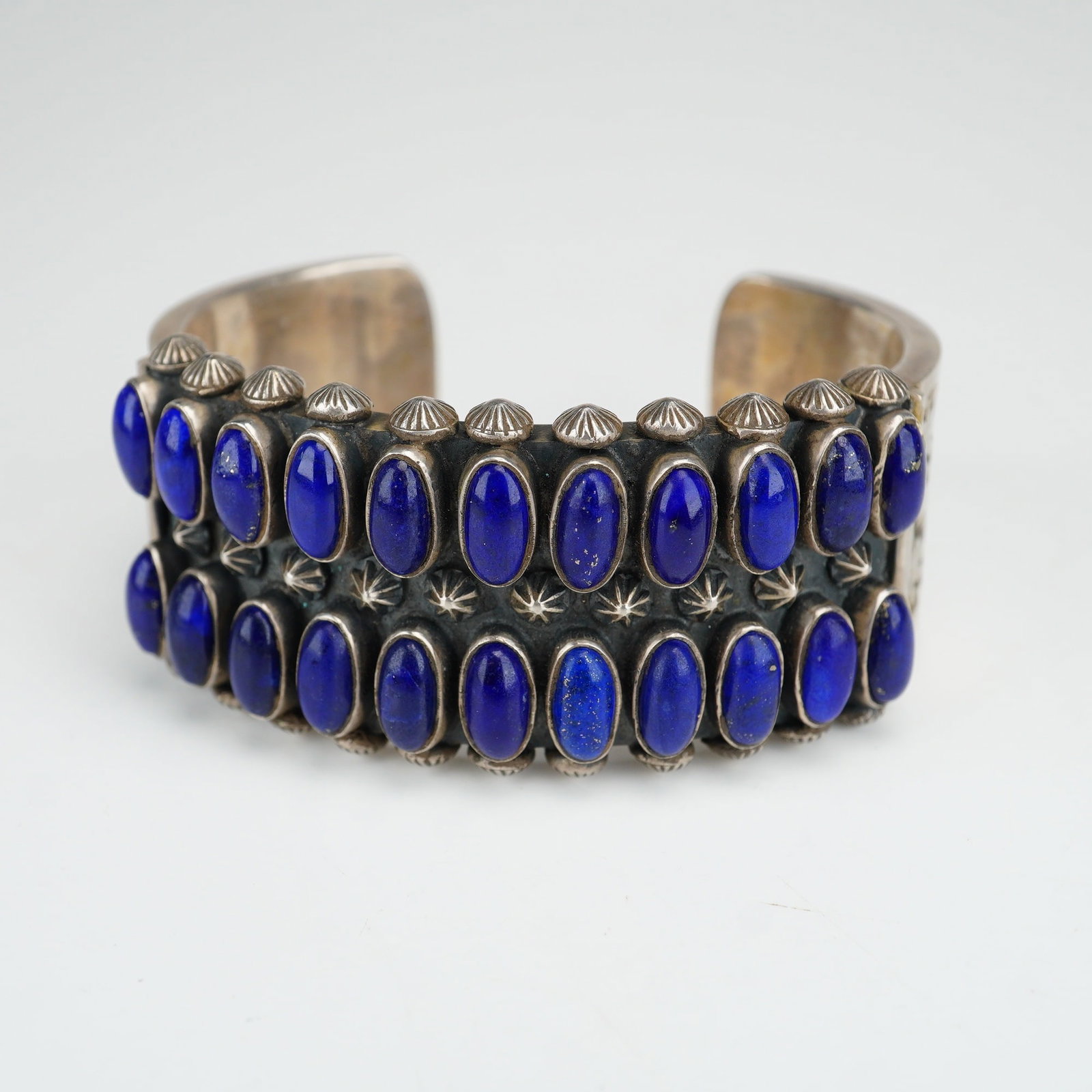 DB Navajo Sterling Silver and Lapis Lazuli Cuff Bracelet: This wide sterling silver cuff bracelet is a contemporary Native American jewelry piece. The exterior of the cuff features bezel-set, oval lapis lazuli cabochons arranged in two parallel rows. The sil
