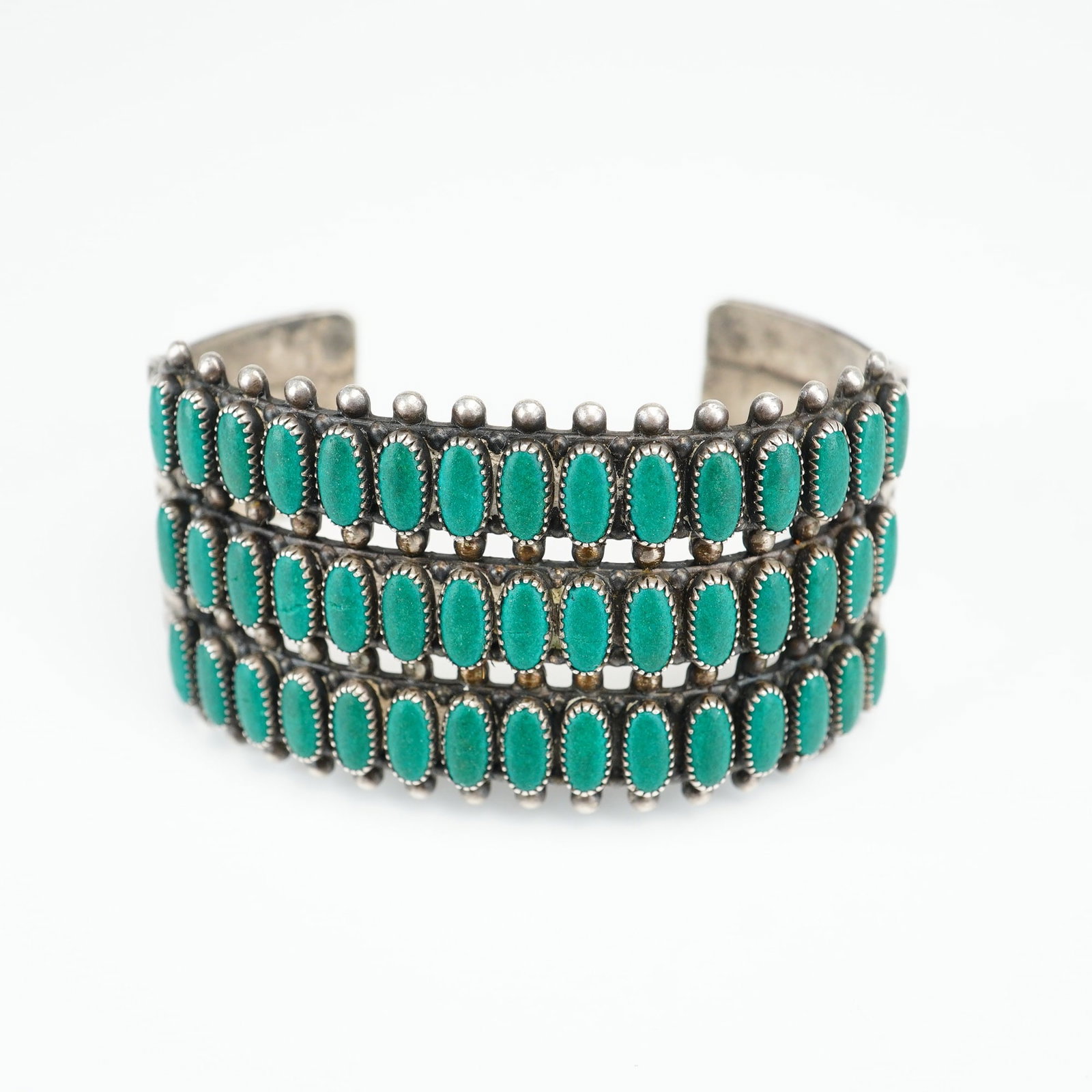 Native American Sterling Silver and Turquoise Petit Point Three Row Cuff Bracelet: This Native American Zuni petit point cuff bracelet is crafted from sterling silver and features three parallel rows of oval-shaped turquoise cabochons. Each of the stones is secured in an individual 