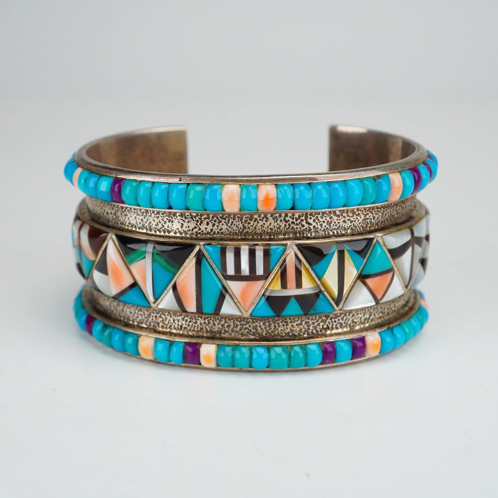 Native American Sterling Silver Multi-Stone Inlay Cuff Bracelet: A contemporary Native American cuff bracelet crafted in sterling silver. The wide cuff features a triple-band construction with elaborate multi-stone inlay. The upper and lower bands are channel-set w