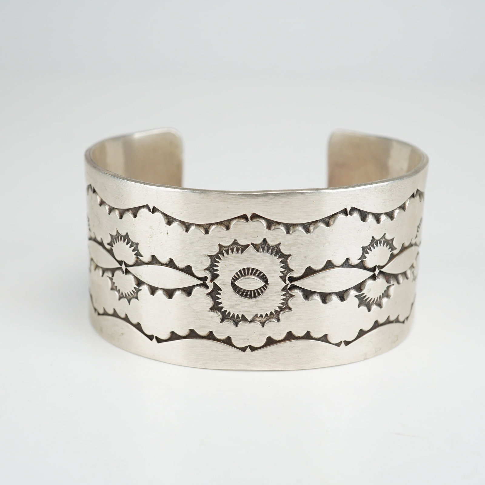 Native American Sterling Silver Stamped Wide Cuff Bracelet: This wide cuff bracelet is crafted from sterling silver and features elaborate stamped ornamentation in the Native American style. The design is characteristic of Navajo silverwork, featuring a wide, 