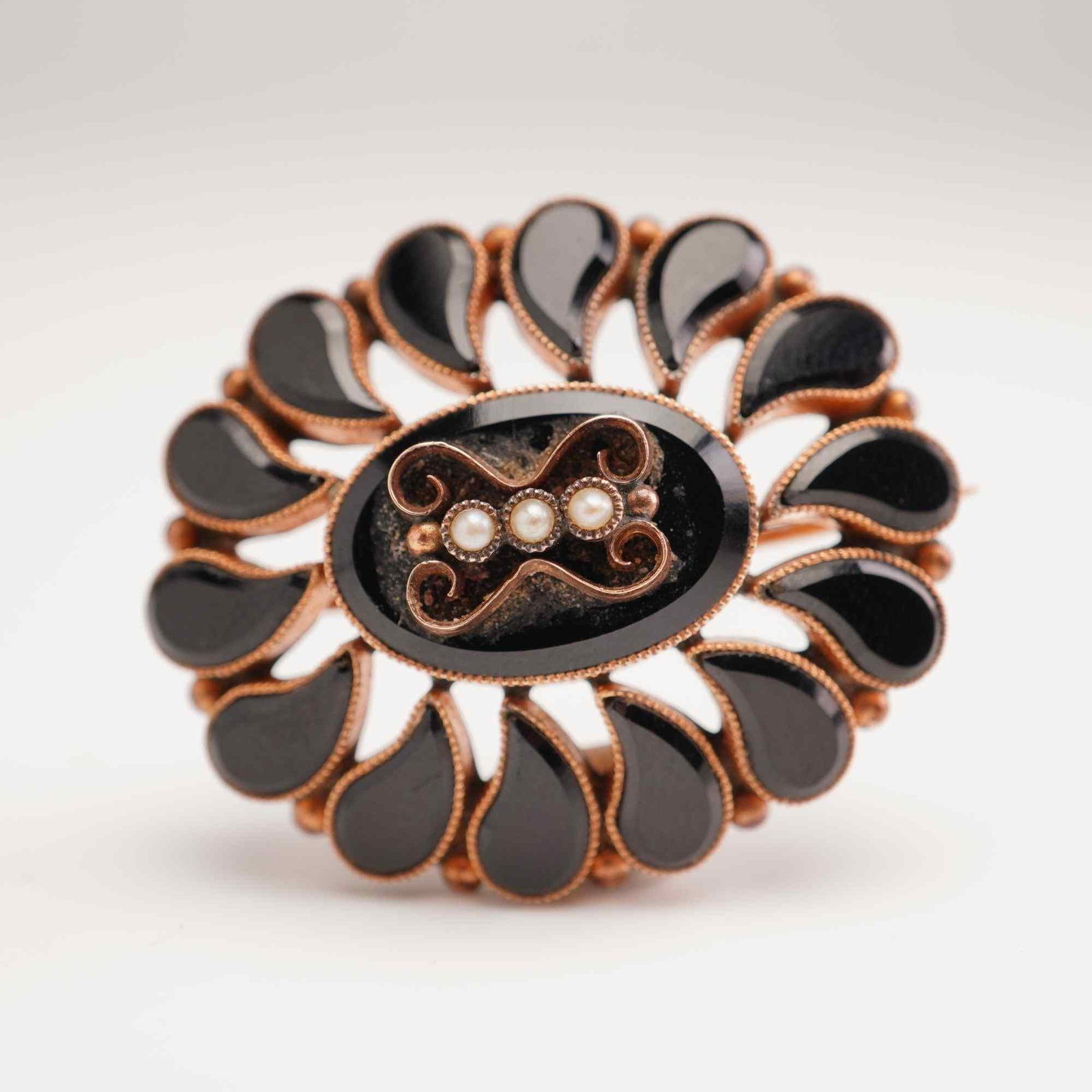 Edwardian 10K Gold Black Onyx and Seed Pearl Brooch: This Edwardian commemorative brooch is crafted from 10 karat gold and features a central oval black onyx cabochon. The center is ornamented with an applied gold filigree scrollwork motif set with thre