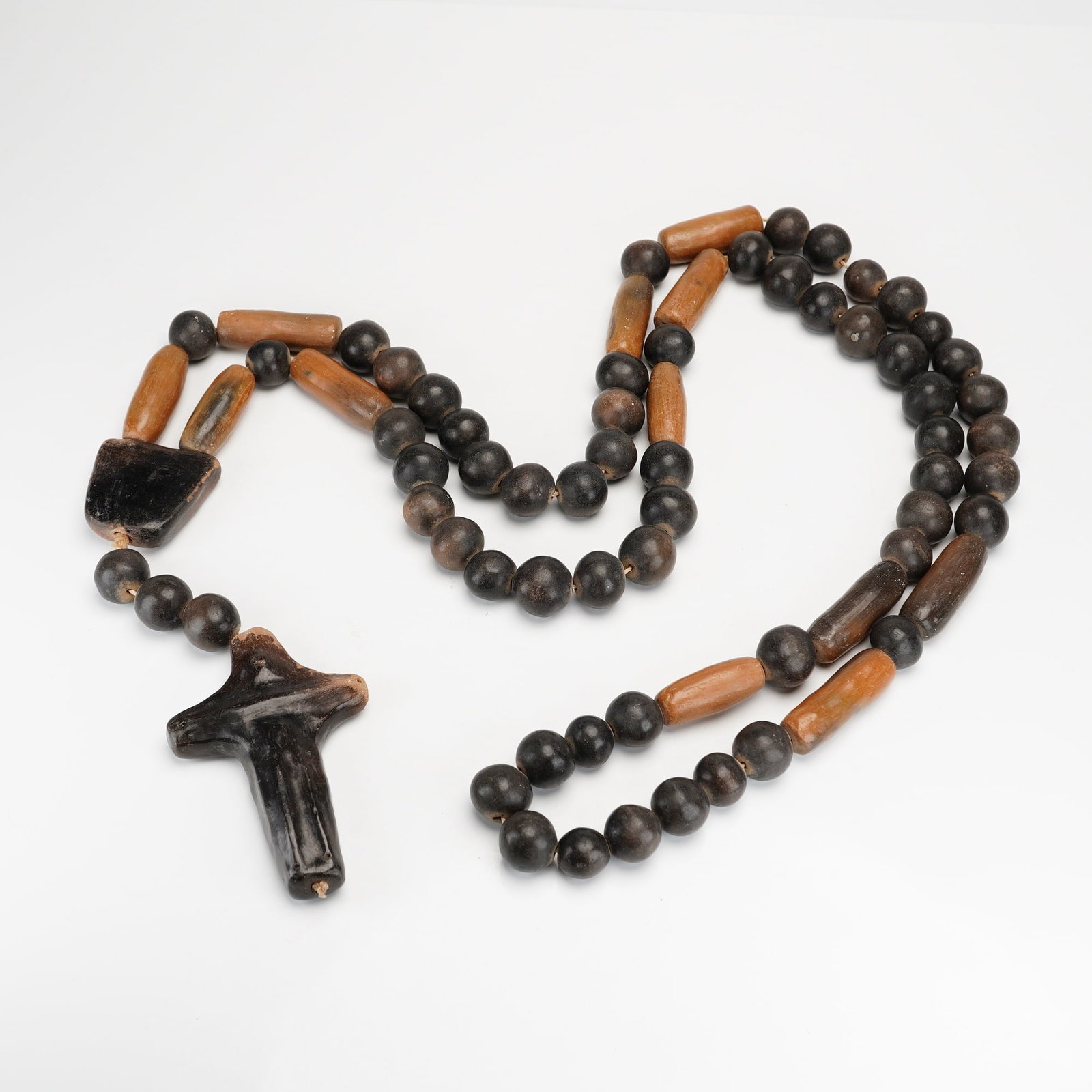 Brazilian Umbanda Handmade Wooden Prayer Beads with Cross Pendant: Featuring a combination of spherical dark brown to black beads and elongated cylindrical beads in a lighter brown tone. The assembly includes a stylized irregularly shaped cross pendant and a