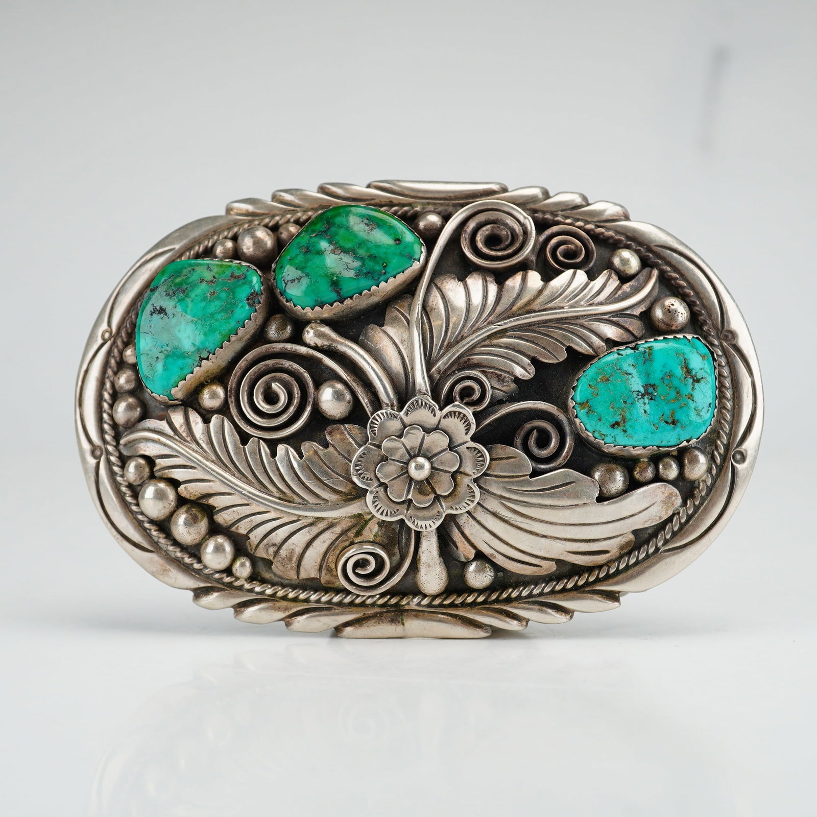 Navajo Sterling Silver and Turquoise Floral Belt Buckle Stamped JL: This Navajo sterling silver belt buckle features a traditional Southwestern floral and foliate motif. The design is centered around a multi-petaled flower flanked by two large, detailed feathery