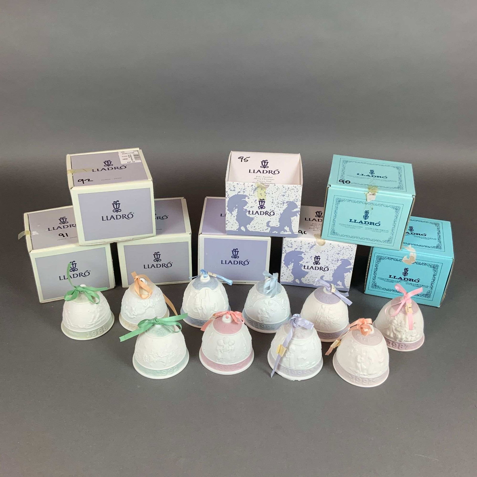 Set of Ten Lladro Annual Porcelain Christmas Bells, 1987-1996: This collection consists of ten Lladro annual porcelain Christmas bells produced between 1987 and 1996. Each bell is crafted in matte white bisque porcelain and features low-relief molded decorative s