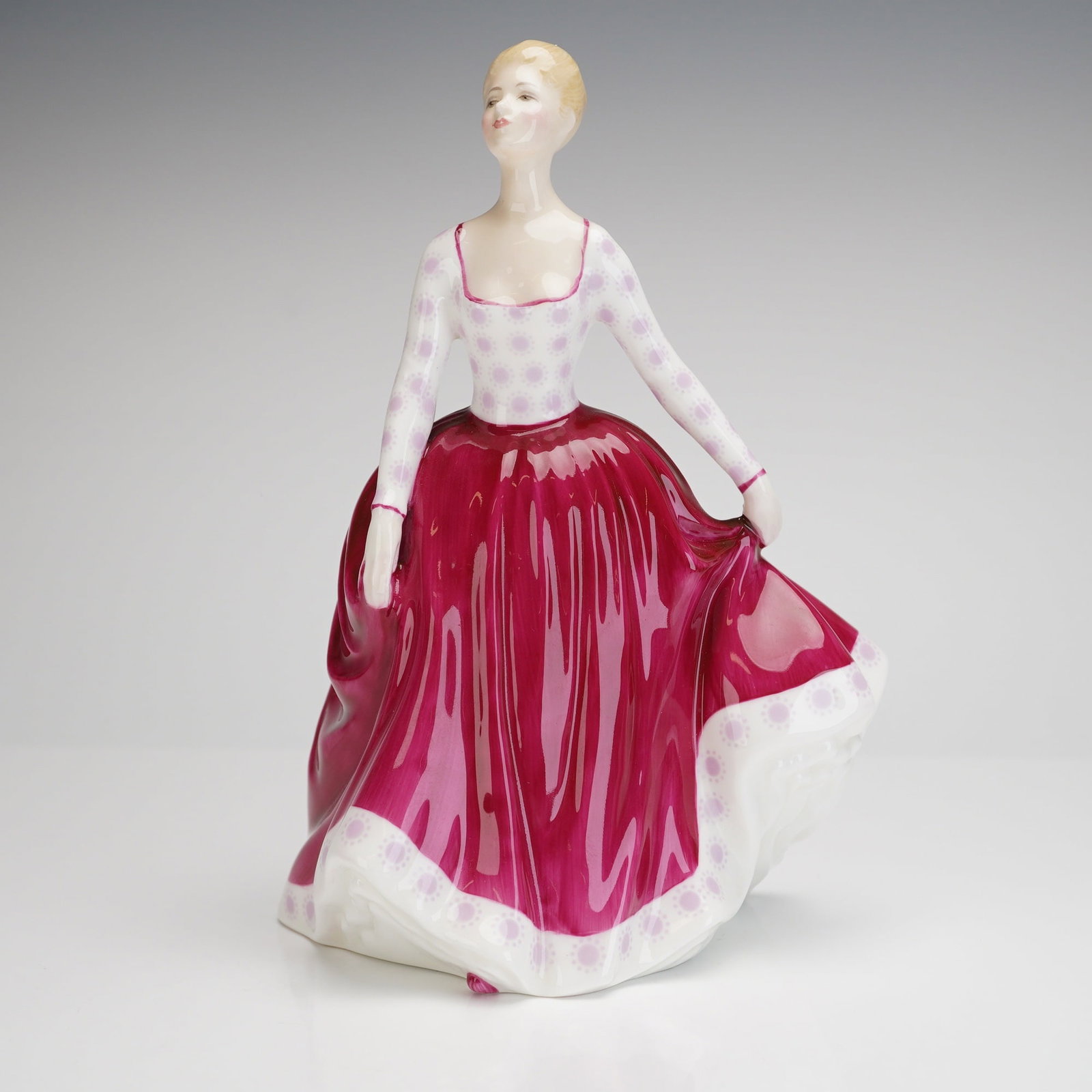 Royal Doulton Figurine Fiona HN 2694: A single glazed bone china figurine manufactured by Royal Doulton, depicting the figure "Fiona." The figure is dressed in a voluminous period gown featuring a high-waisted deep magenta skirt and a whi