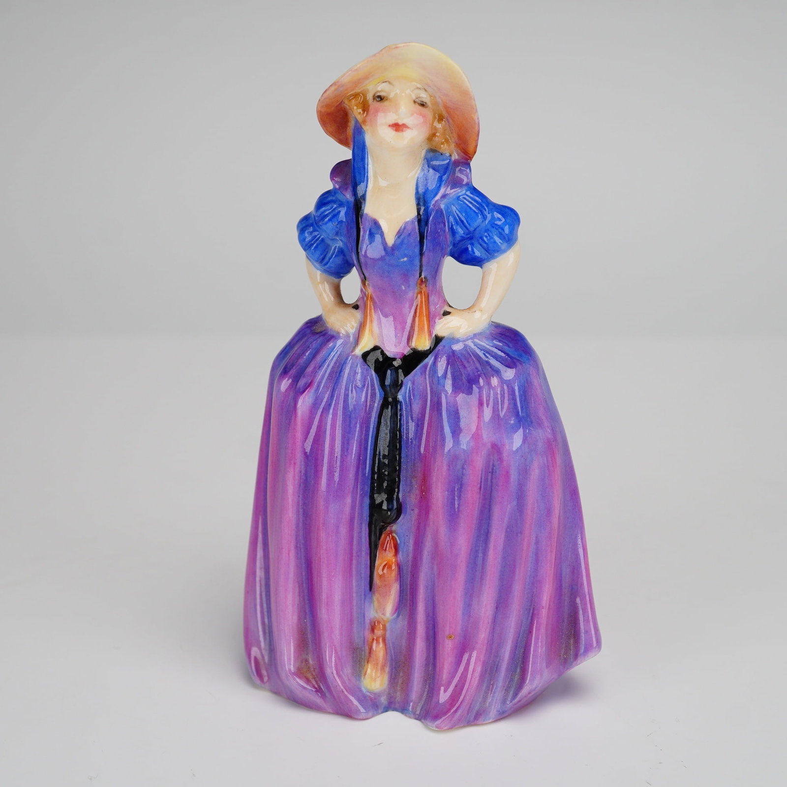 Royal Doulton Figurine, Patricia M28: This Royal Doulton miniature figurine, titled Patricia and designated as model number M28, is a fine example of glazed bone china craftsmanship. The figure portrays a woman in a stylized eighteenth-ce