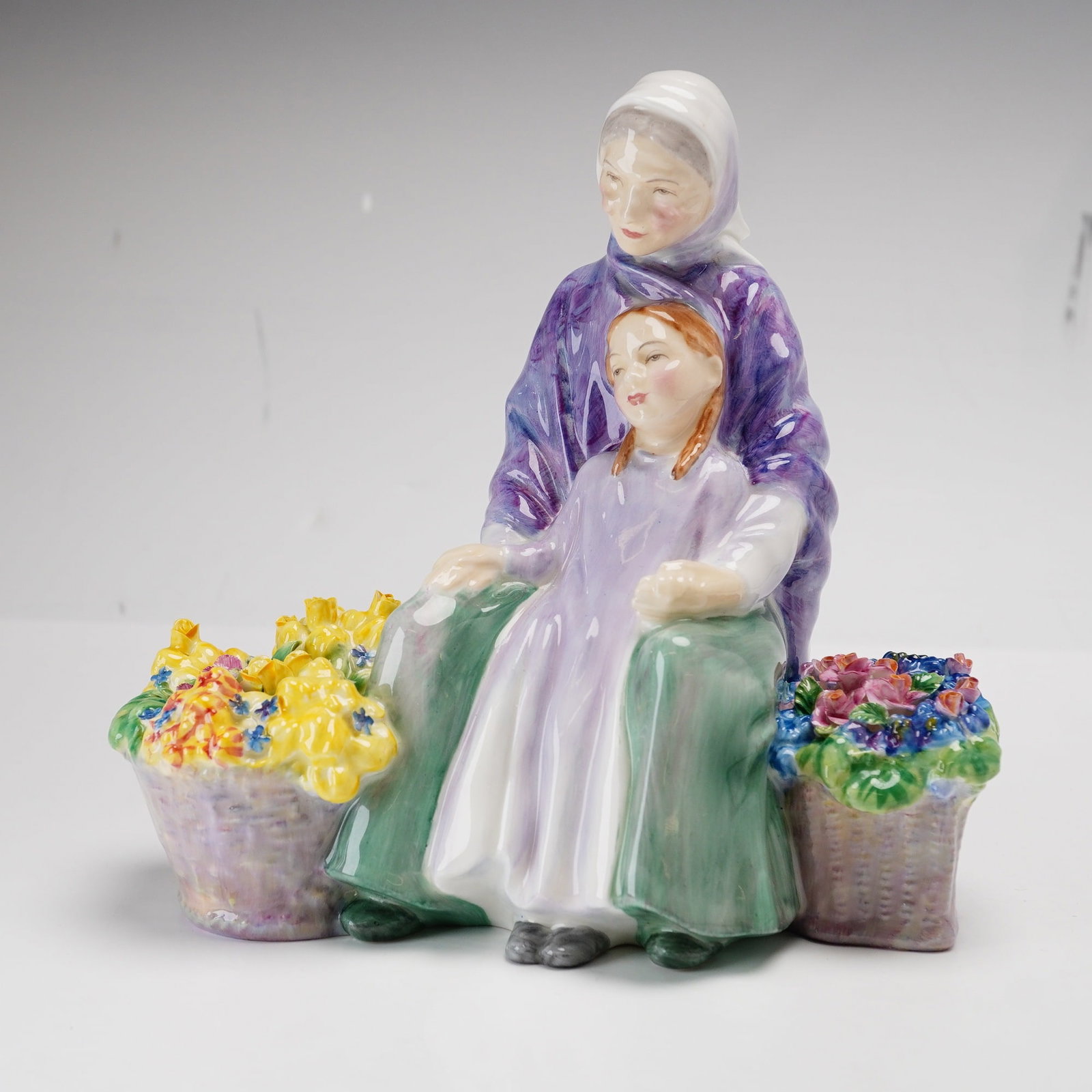 Royal Doulton Bone China Figurine Granny's Heritage HN2031: This Royal Doulton bone china figurine, titled Granny's Heritage, is model number HN 2031. The piece depicts an elderly woman and a young girl seated together, flanked by two overflowing baskets of co