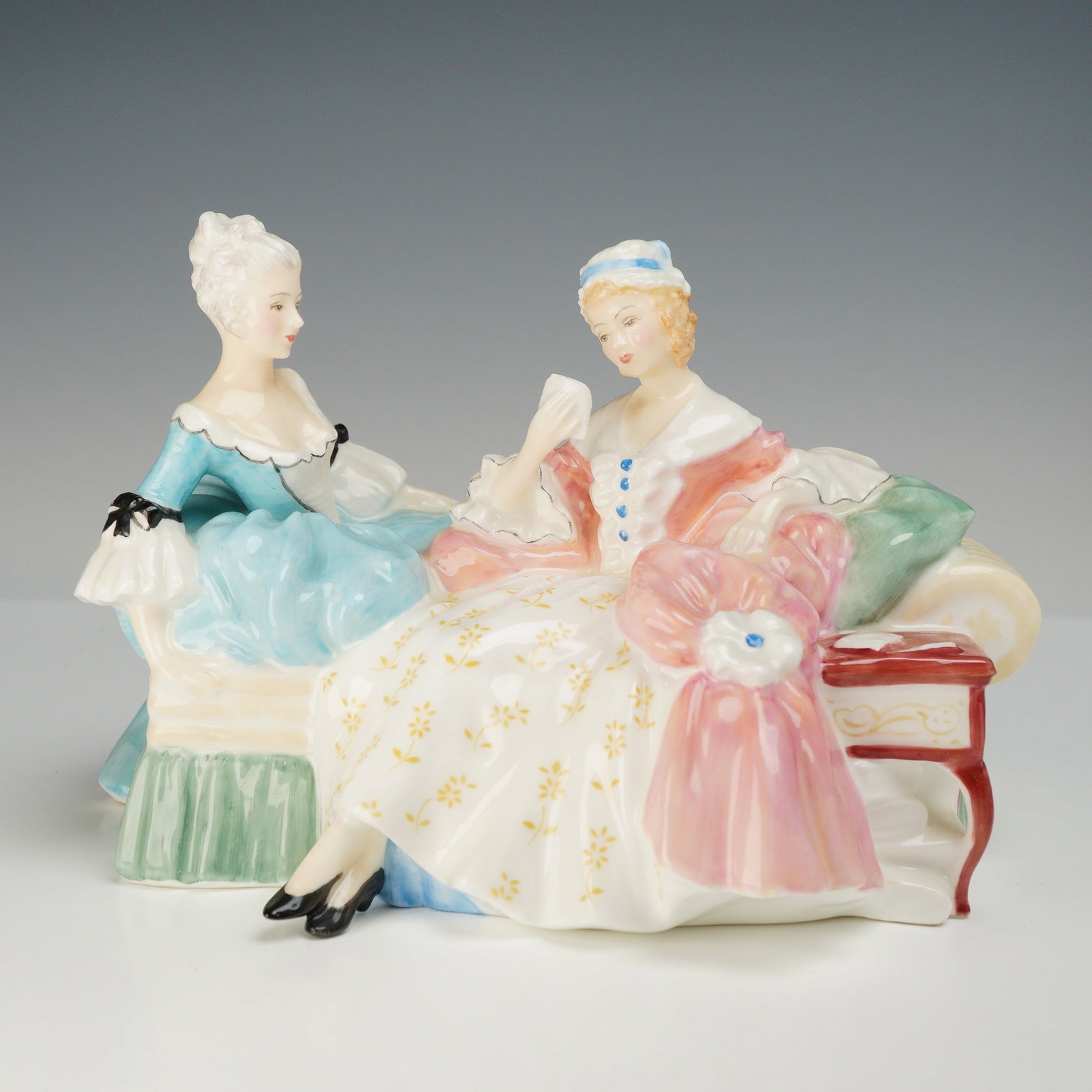 Royal Doulton Bone China Figurine, The Love Letter HN2149: Depicts two women in 18th-century style dress seated on a rococo-style settee. One figure wears a light blue gown with black ribbon accents, while the other is dressed in a white gown with yellow flor