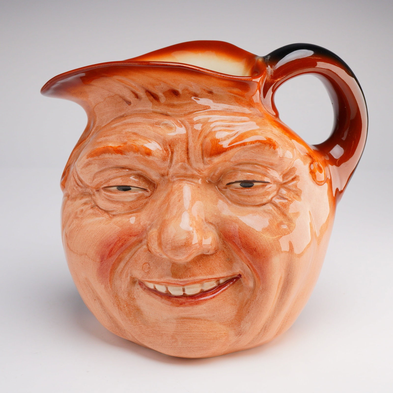 Royal Doulton Large Character Jug, John Barleycorn D5327: The single ceramic jug is modeled in the style of a Toby jug, depicting the face of a smiling elderly man with deeply wrinkled features. The piece is finished in a high-gloss reddish-brown and tan gla