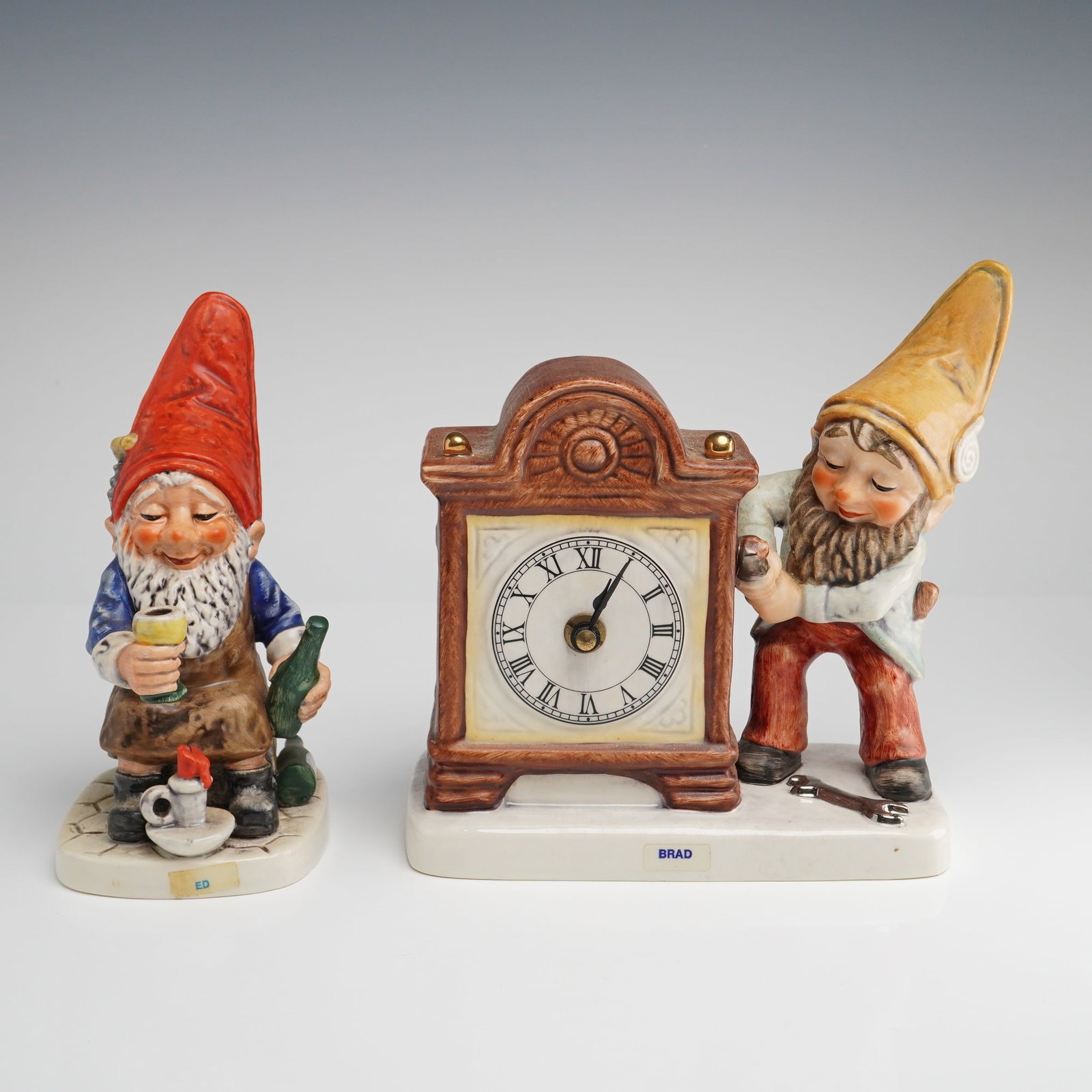 Goebel Co-Boy Gnomes, Ed the Drinker and Brad the Clockmaker Figural Clock: A pair of vintage Goebel Co-Boy ceramic gnome figurines, manufactured in West Germany. This lot includes Ed the Drinker, model Well 503, and Brad the Clockmaker, model 17 506 18. Ed is depicted in a j