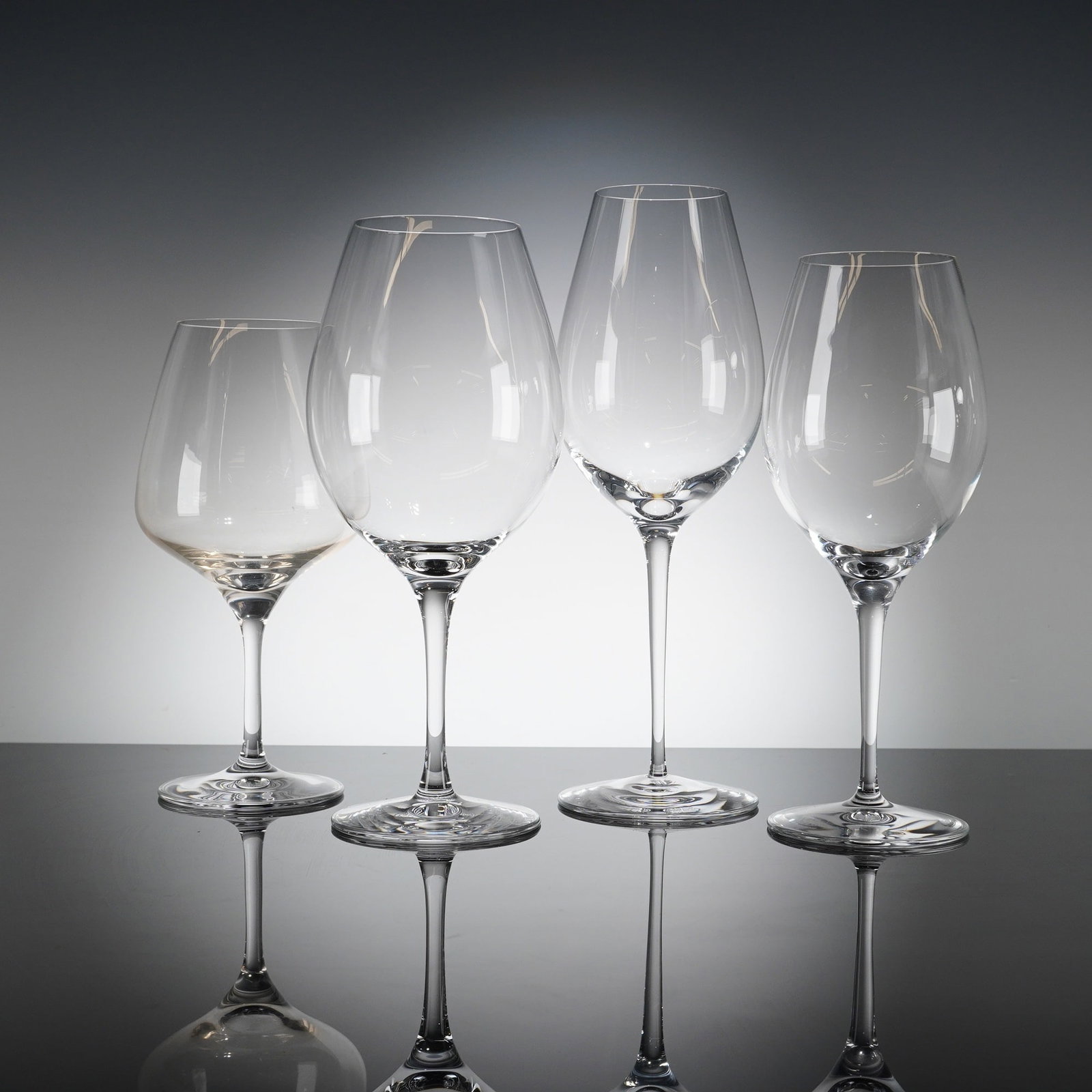A Collection of Four Orrefors More Crystal Wine Glasses: A collection of four contemporary stemmed drinking glasses identifi?ed as the Orrefors More Wine patern. The glasses are crafted from clear crystal, featuring fi?nely blown bowls of varying shapes and
